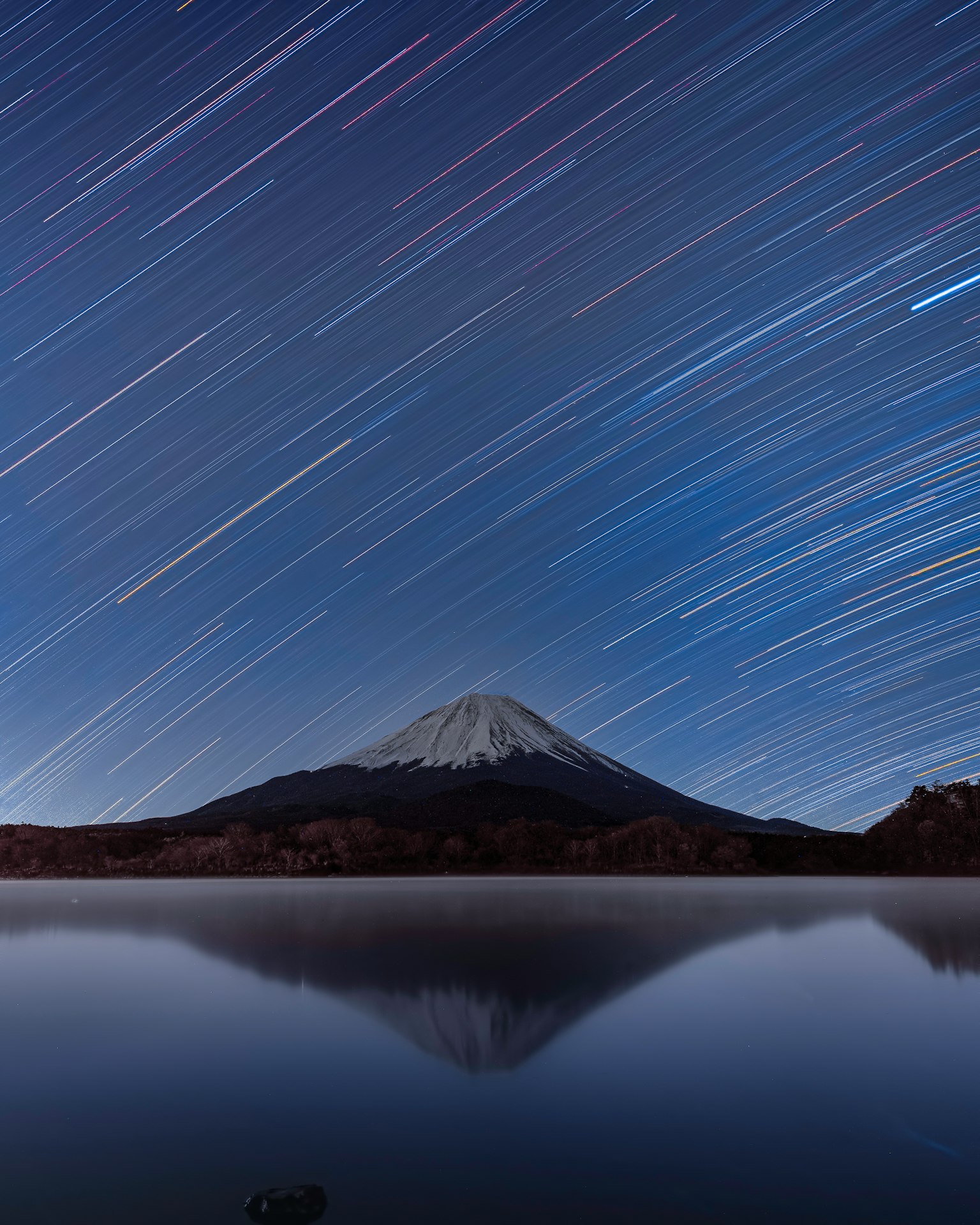 Long exposure photo of Mount Fuji with star trails and a reflective water surface
