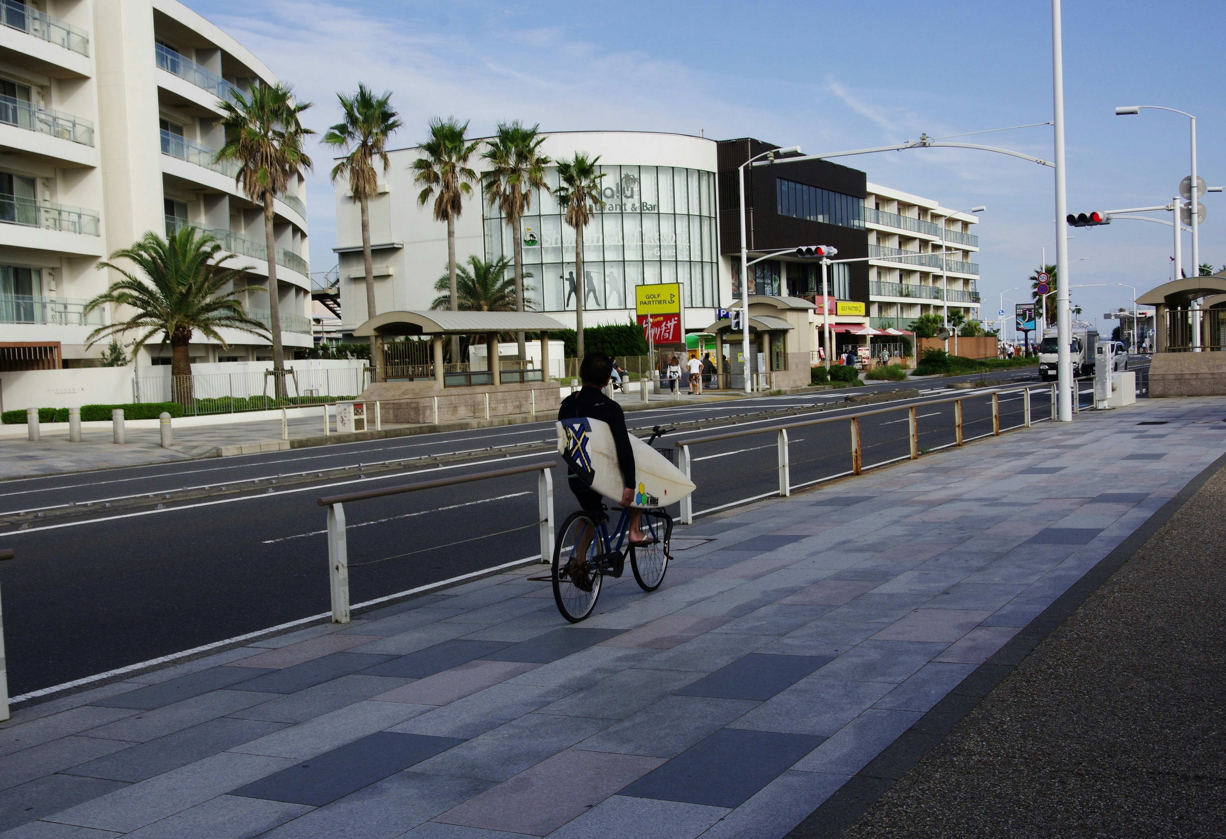 湘南の街で自転車に乗る人とサーフボードのある風景