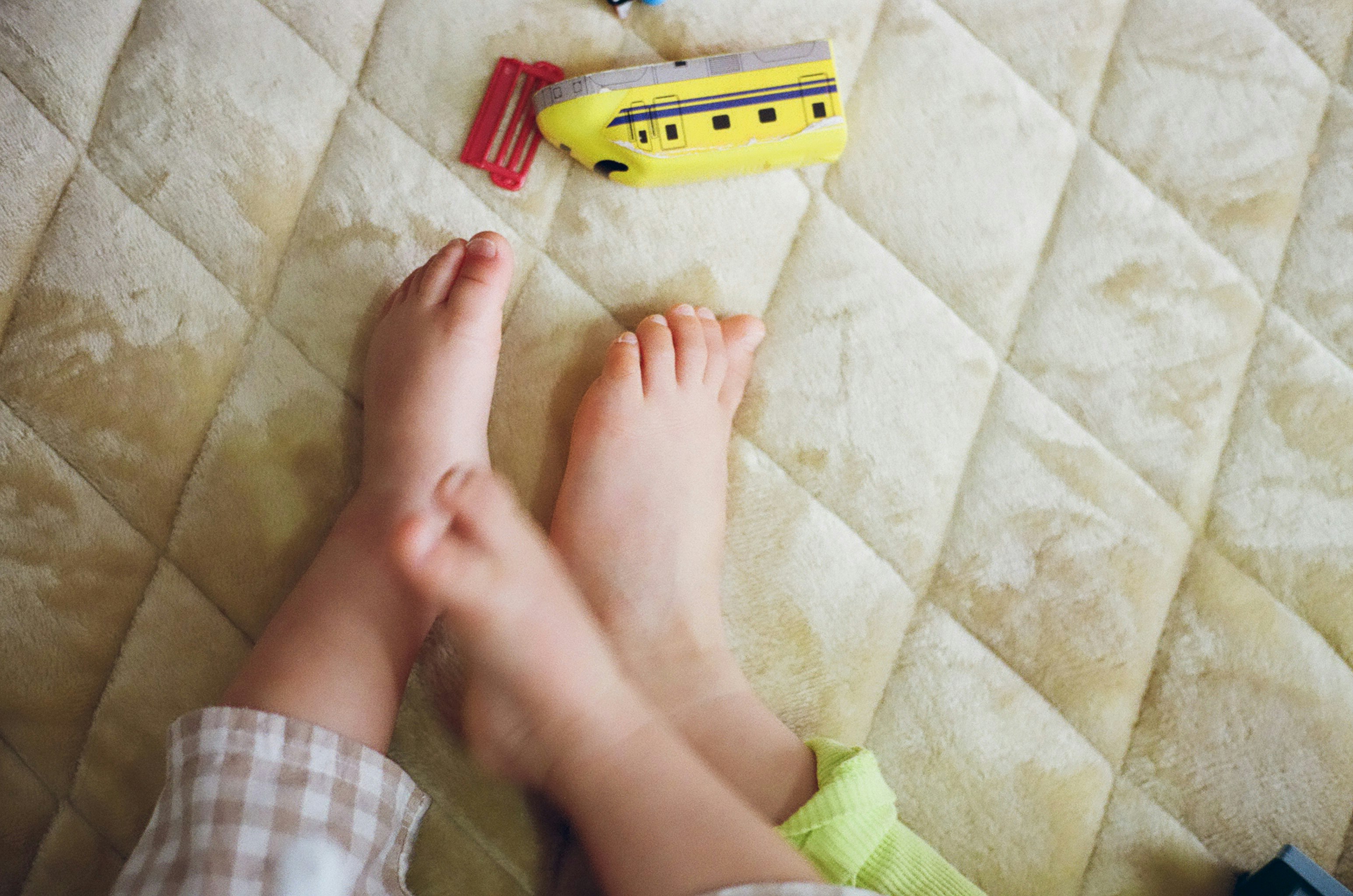 Children's feet with a yellow toy submarine on a quilted bed