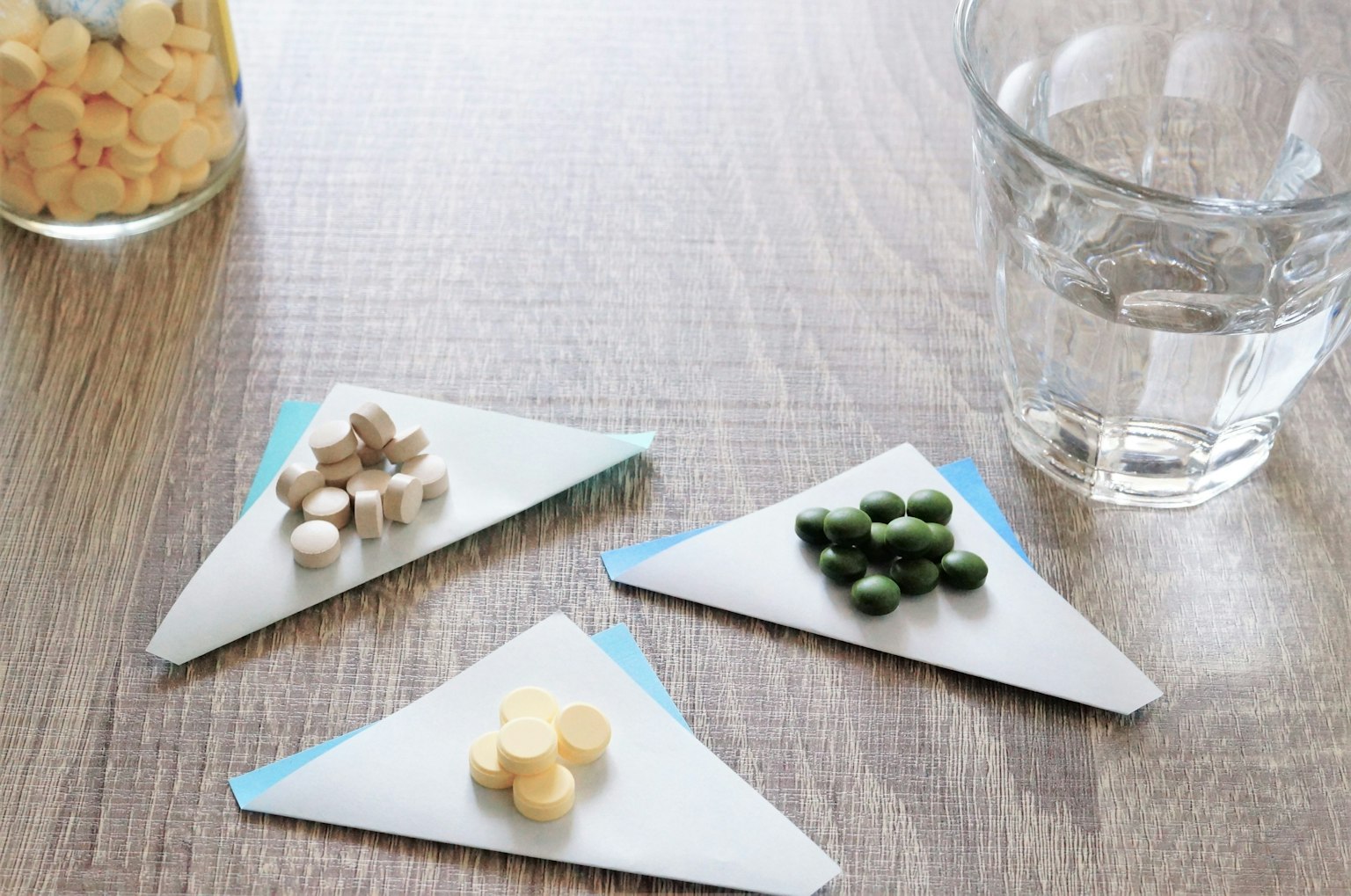 Integratori disposti su carta triangolare con un bicchiere d'acqua