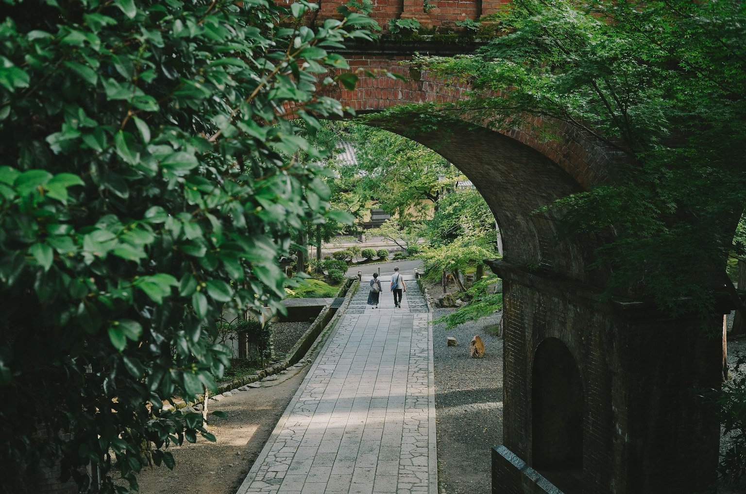 Personas caminando por un camino de piedra bajo un arco verde