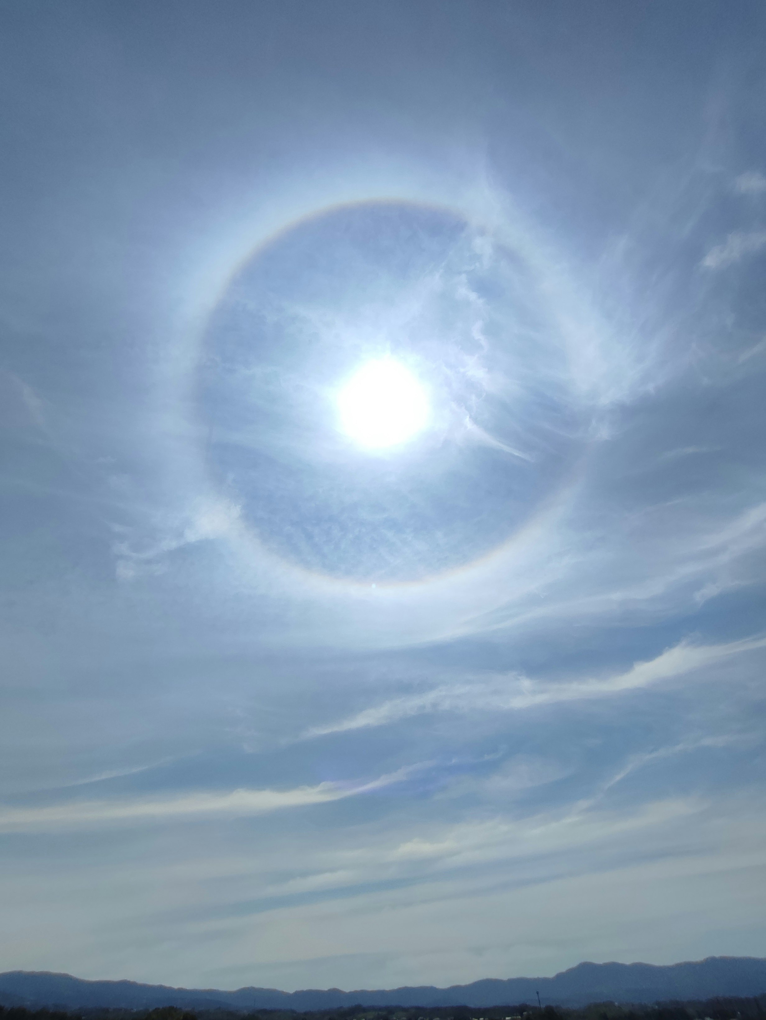 halo solar en el cielo azul con nubes y cordillera al fondo