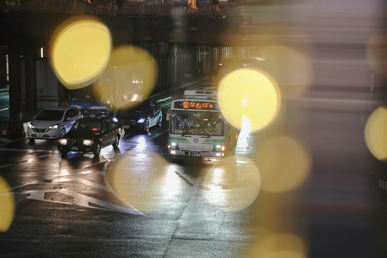一輛公車和幾輛汽車在雨中穿過交叉口，背景是模糊的燈光