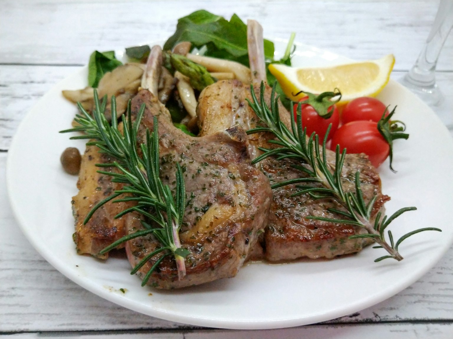 Chuletas de cordero a la parrilla adornadas con romero servidas con ensalada y limón