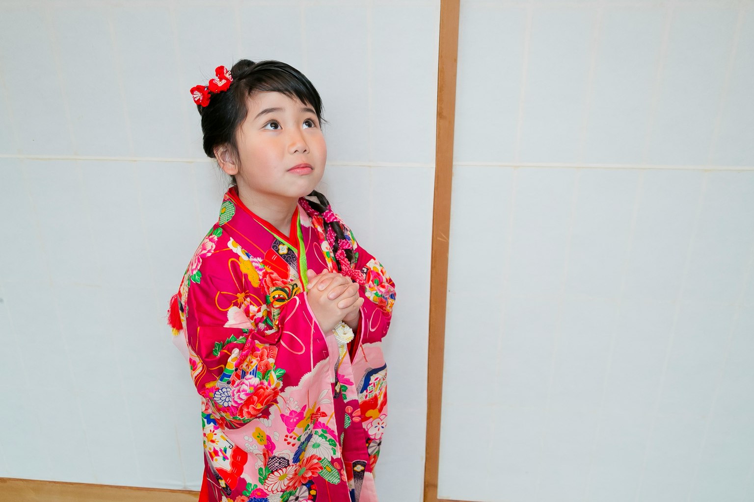 Gadis mengenakan kimono bunga cerah berdiri di depan latar belakang putih