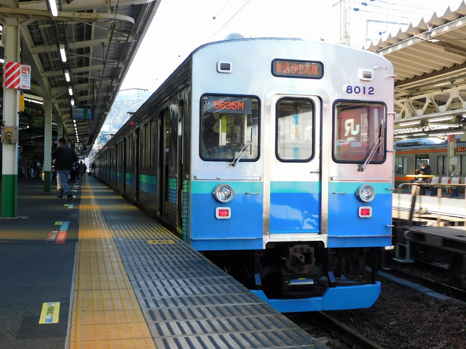 Un train bleu arrêté à une station avec une plateforme à proximité et une signalisation visible