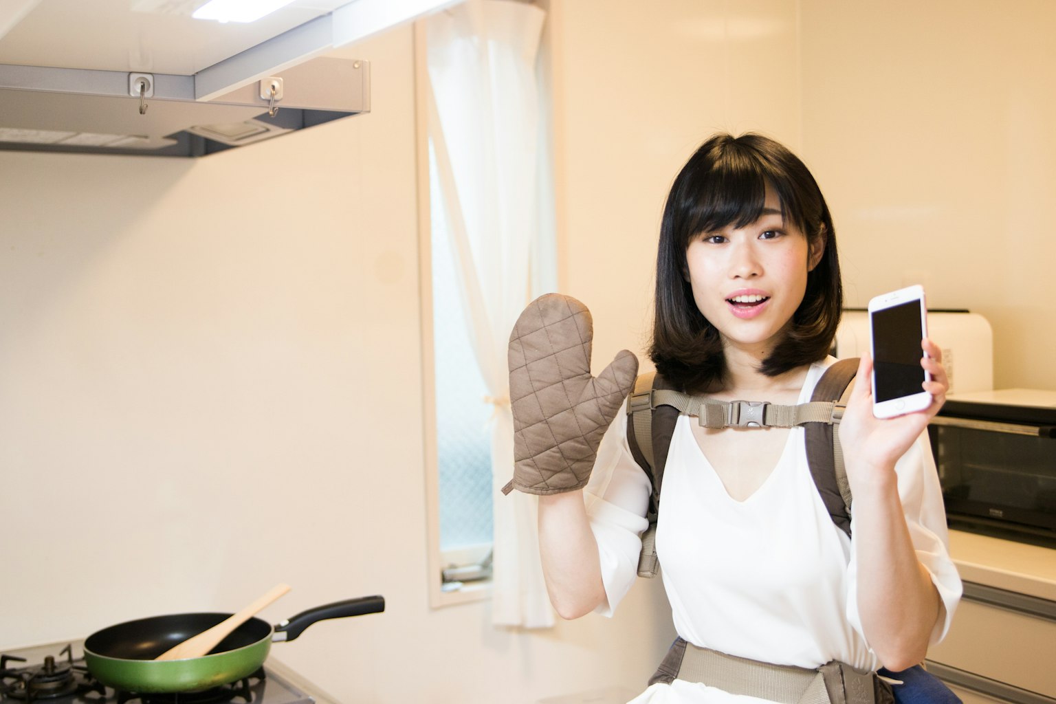 Mujer en la cocina sosteniendo un teléfono inteligente y usando un guante de cocina