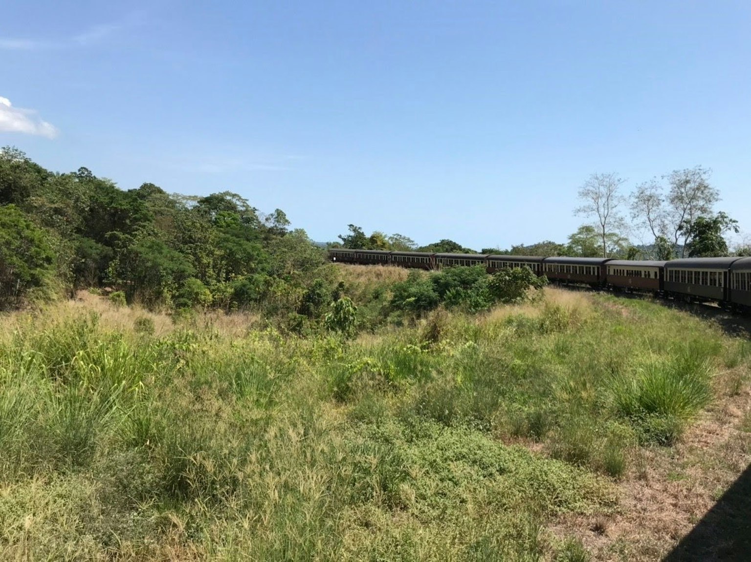 รถไฟโค้งผ่านทุ่งหญ้าสีเขียวและท้องฟ้าสีฟ้า