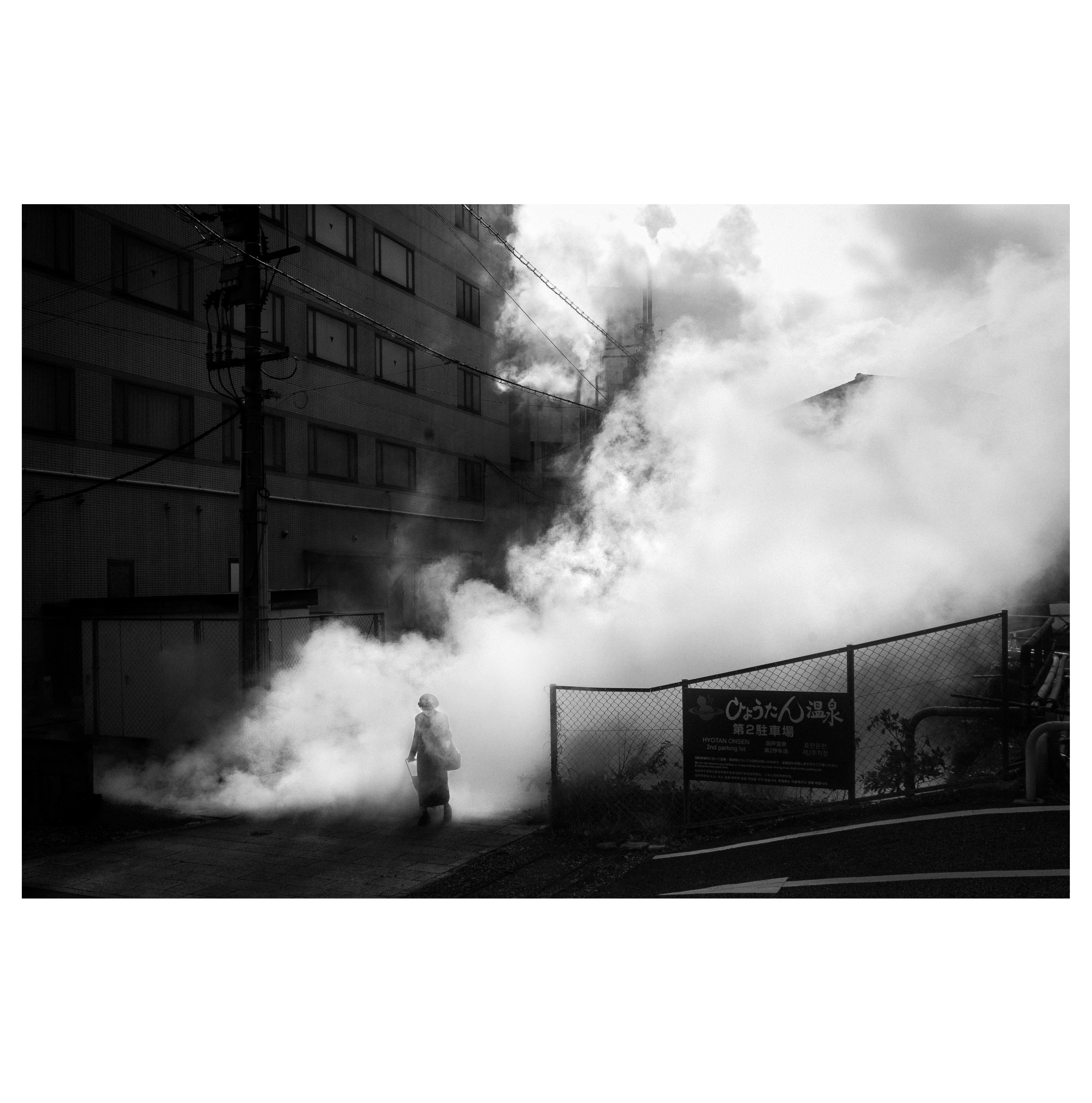 煙に包まれた街角で立つ人物のモノクロ写真