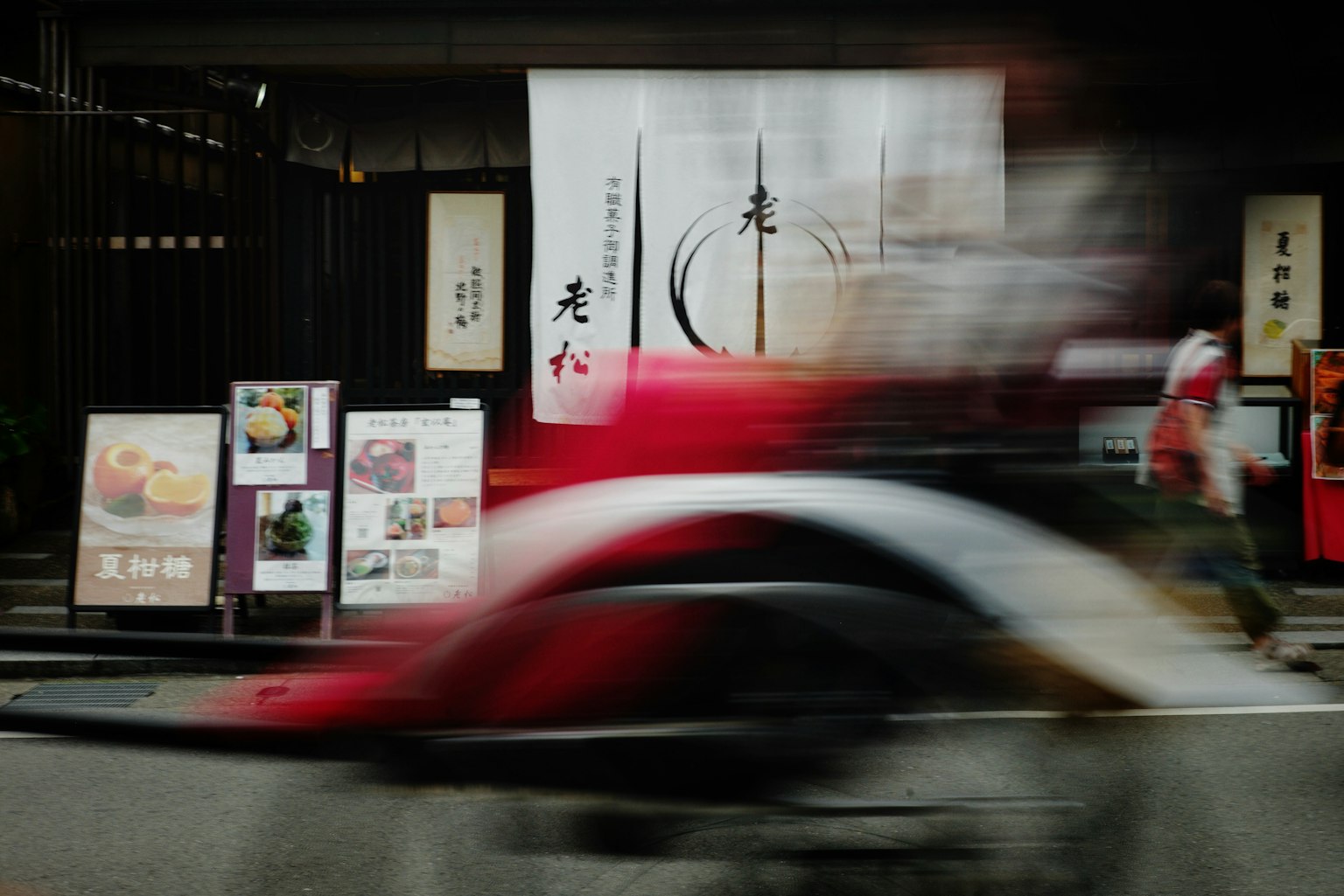 Ein rotes Motorrad in Bewegung in einer japanischen Straßenszene mit traditionellen Schildern und Menütafeln im Hintergrund