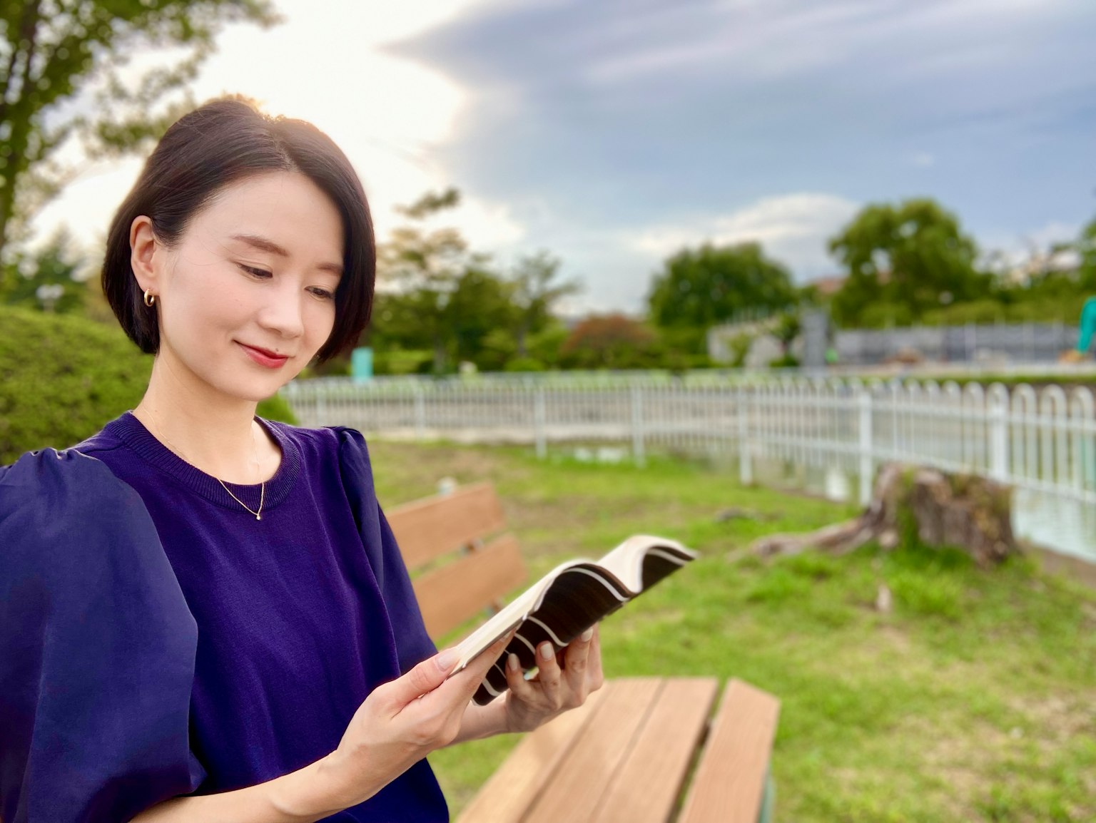 ผู้หญิงอ่านหนังสือในสวน สวมชุดสีน้ำเงิน สีหน้าแสดงความผ่อนคลายในธรรมชาติ