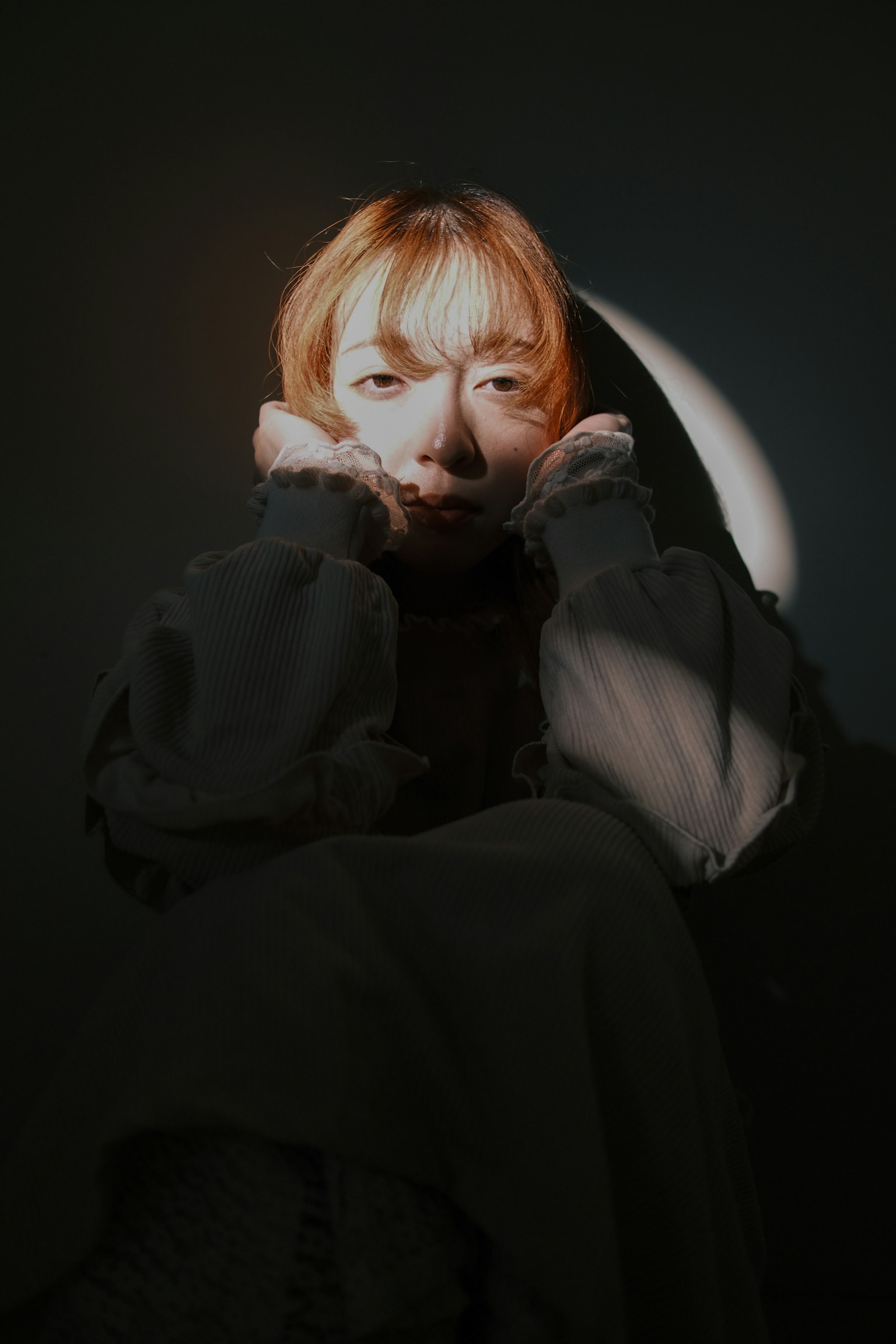 暗い背景に座る女性のポートレート 髪は金色で顔に光が当たる