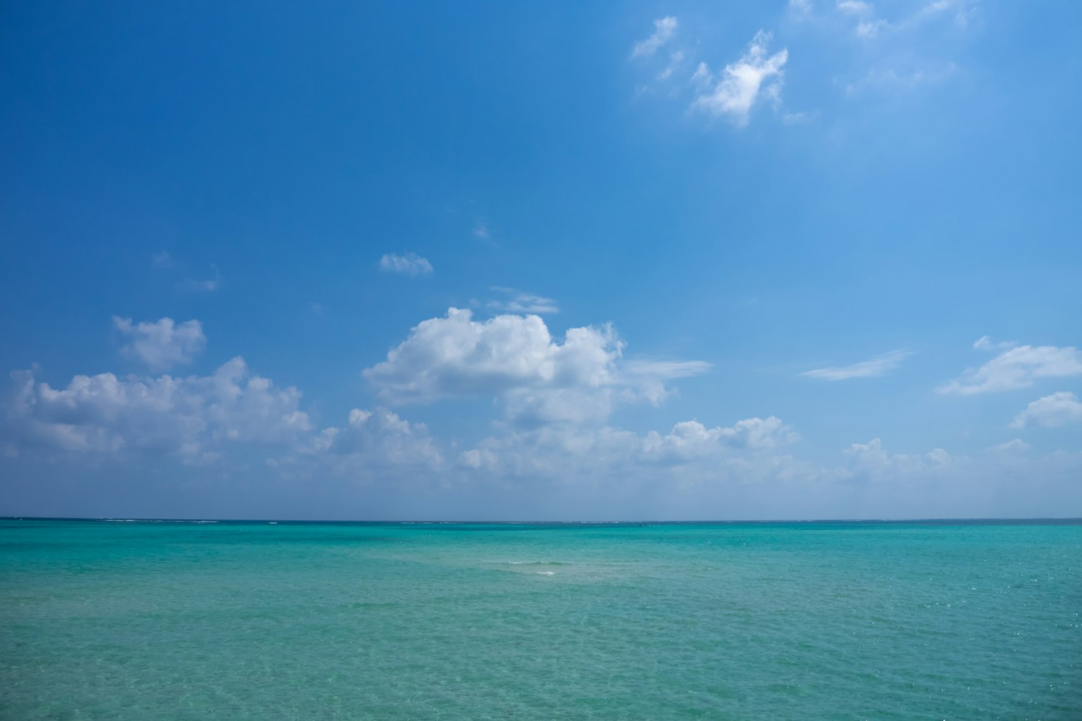 Mar azul claro bajo un cielo brillante con nubes blancas