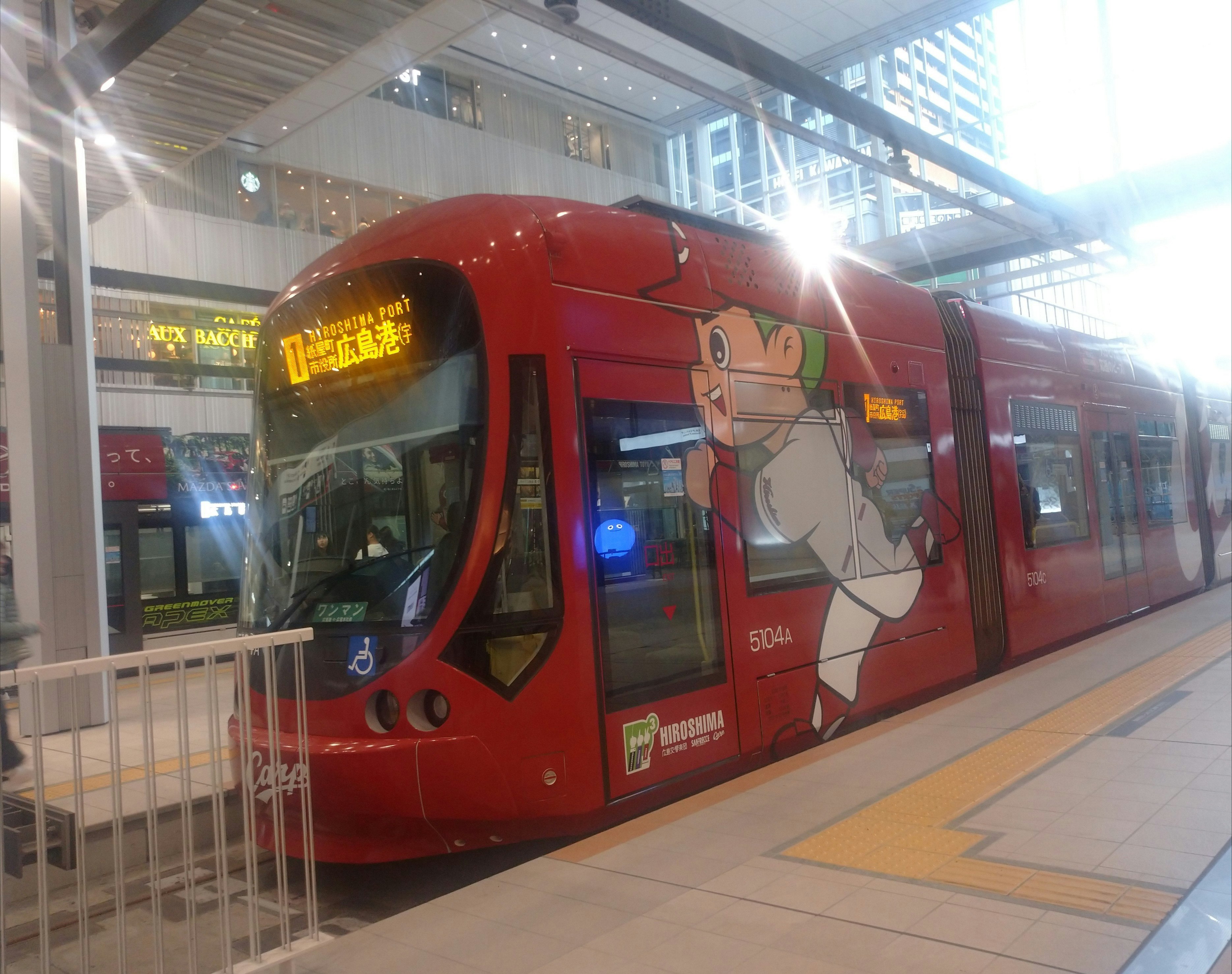 赤い電車と車両側面のアニメラッピングが並ぶ駅のホーム