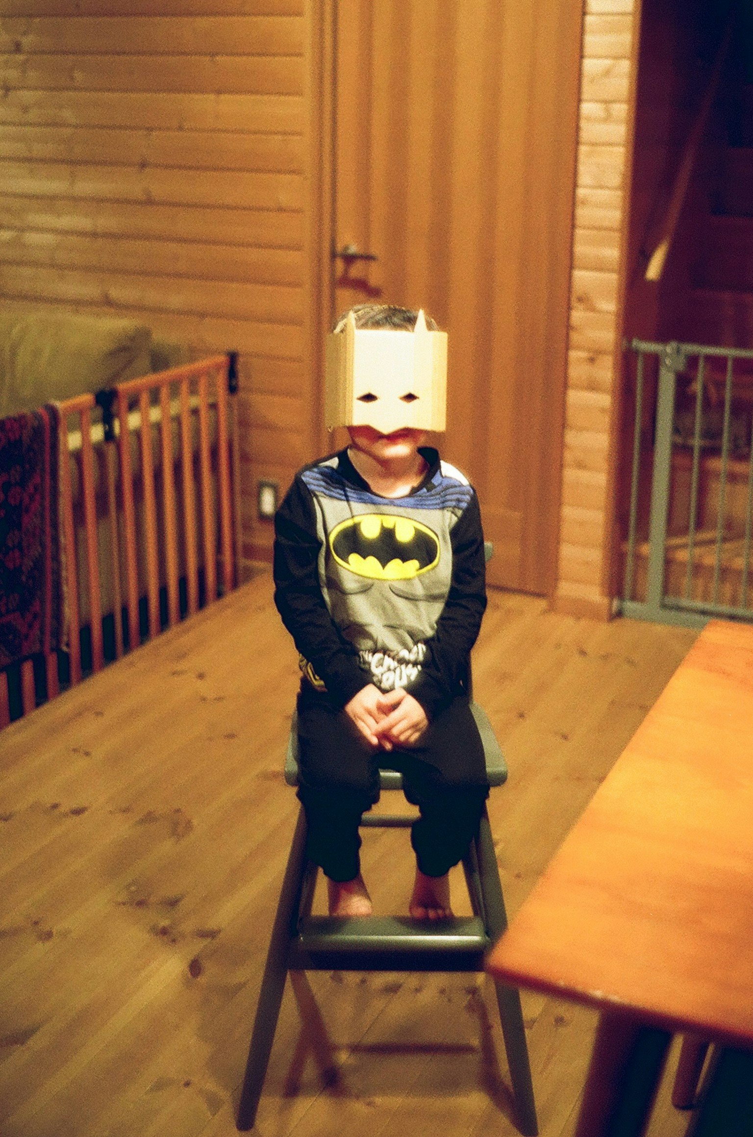 Bambino vestito con pigiama Batman seduto su uno sgabello in una stanza di legno