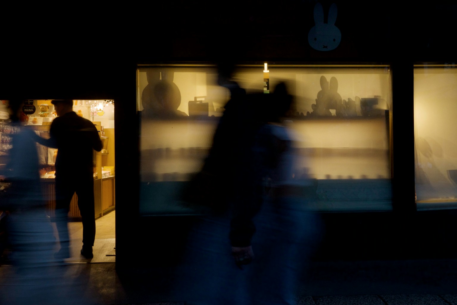 Persone che passano davanti a un negozio poco illuminato con vetrine illuminate