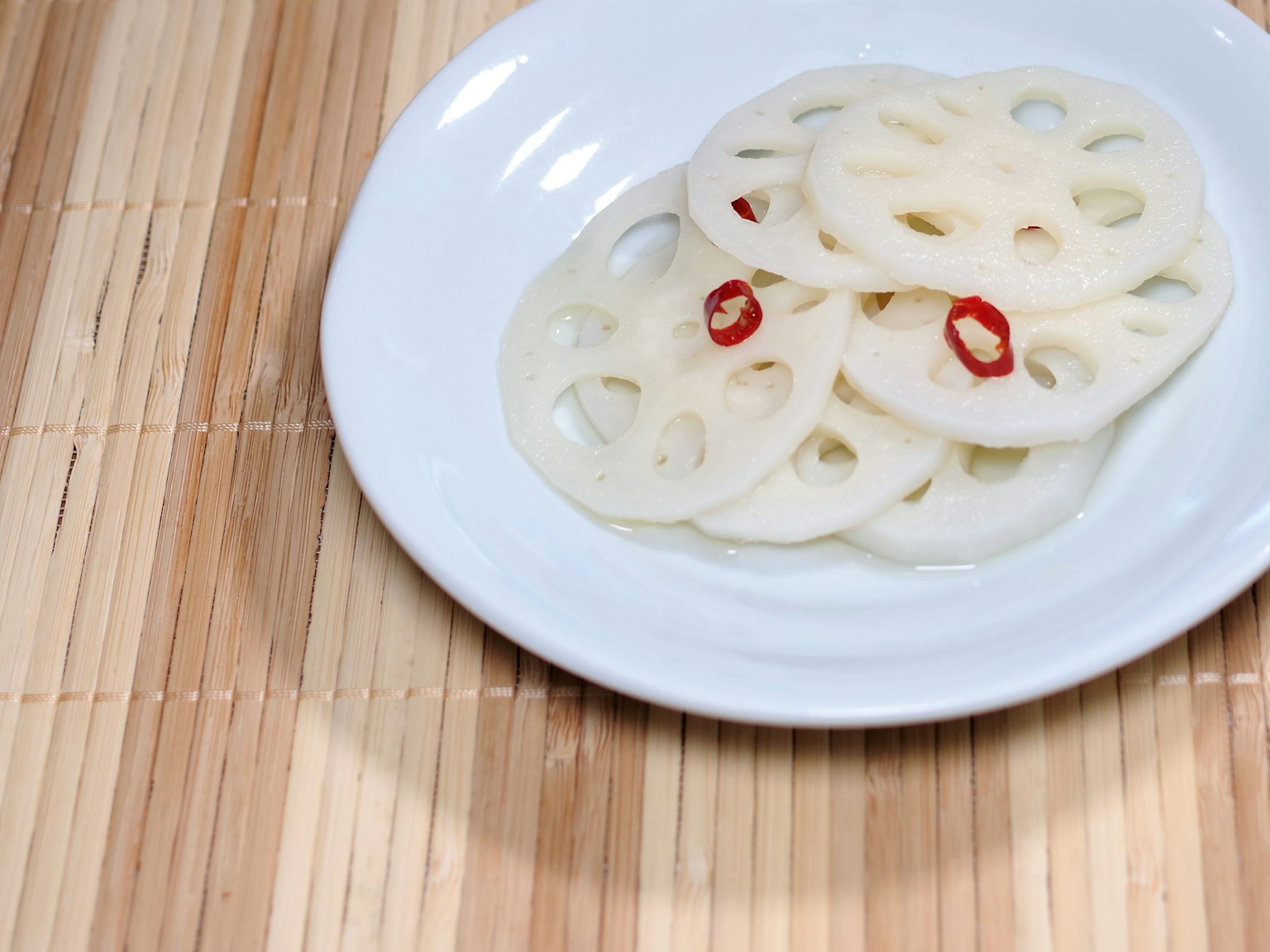 Scheiben von Lotuswurzel mit rotem Chili auf einem weißen Teller