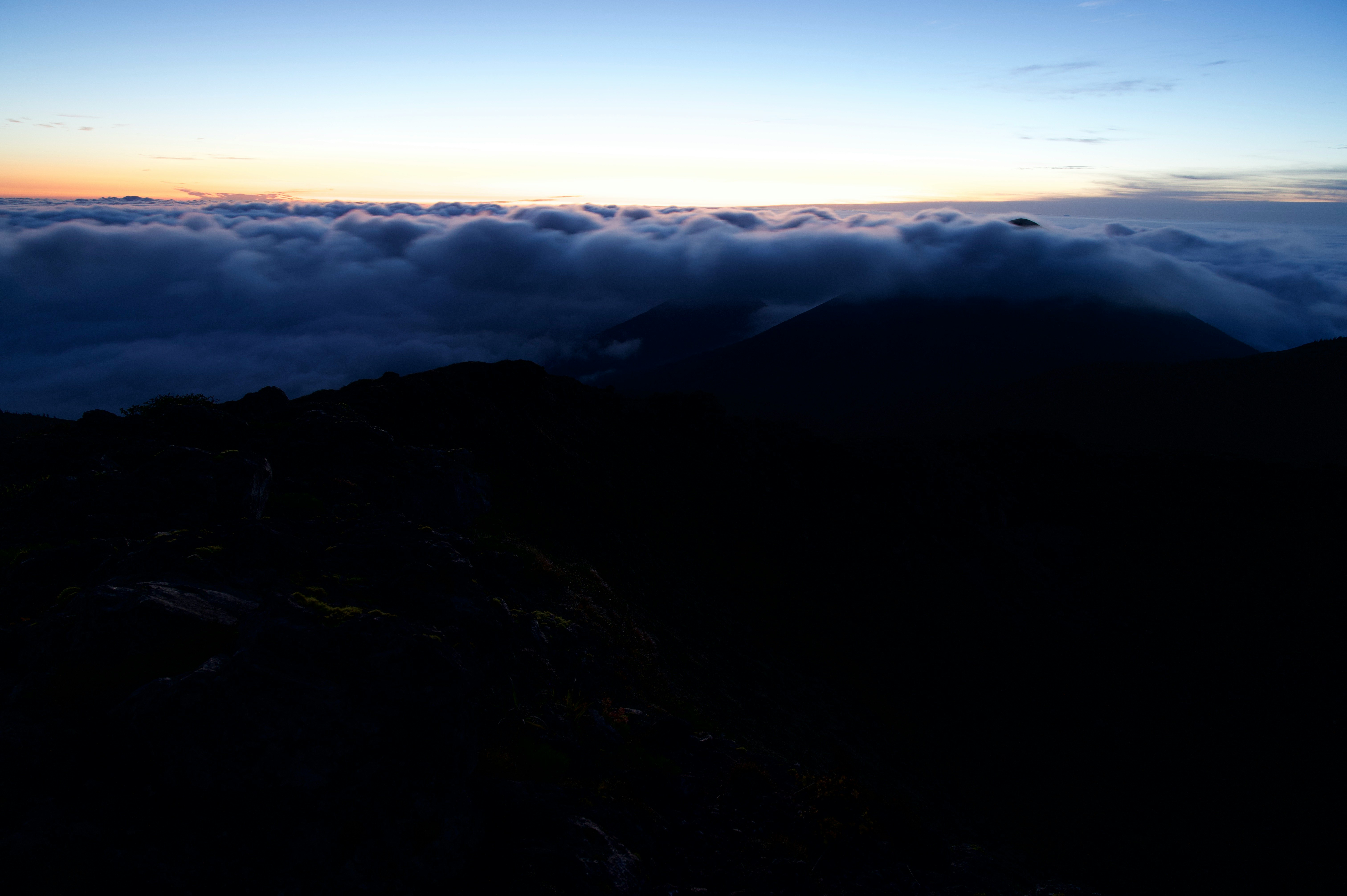 Sonnenuntergangshimmel mit Silhouetten von Bergkämmen über einer Wolkenmeer