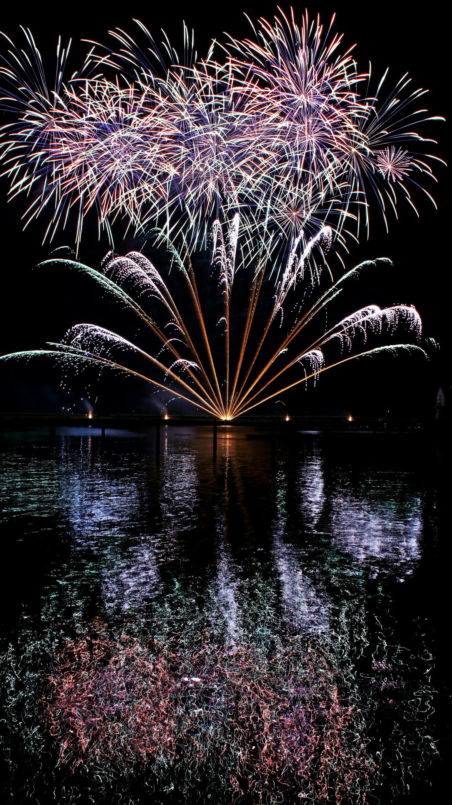 夜空に広がる色とりどりの花火と水面に映る反射