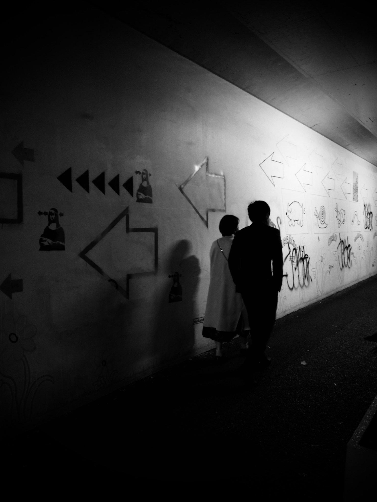Siluet dua orang berdiri di depan grafiti dan panah di dinding terowongan gelap