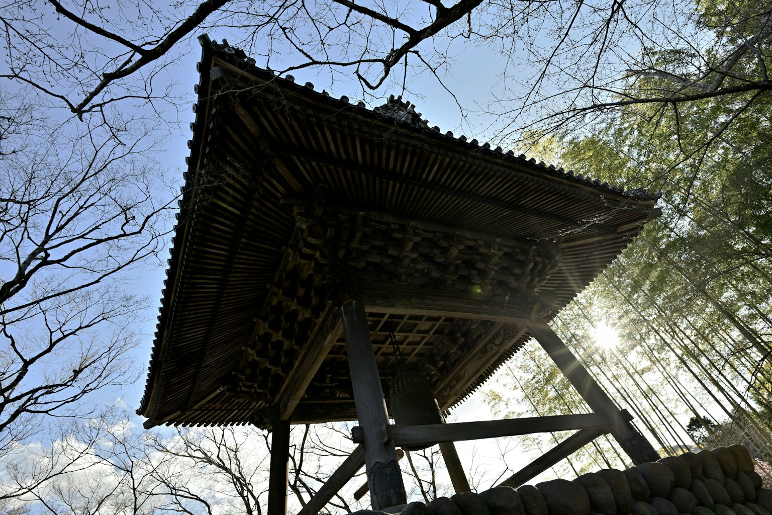 Toit d'un temple en bois vu de dessous avec des arbres en arrière-plan