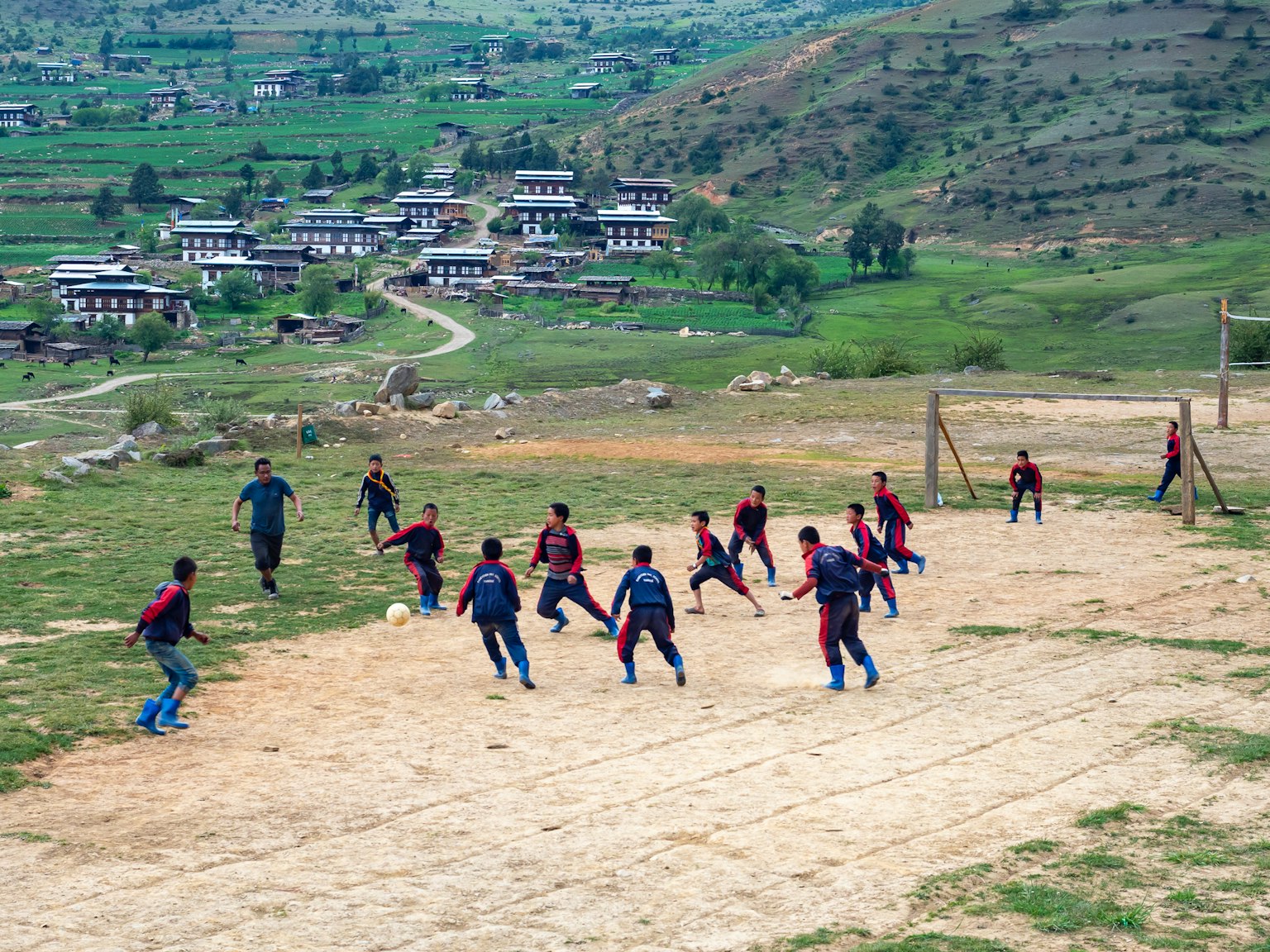 Bambini che giocano a calcio su un campo di terra con colline verdi sullo sfondo