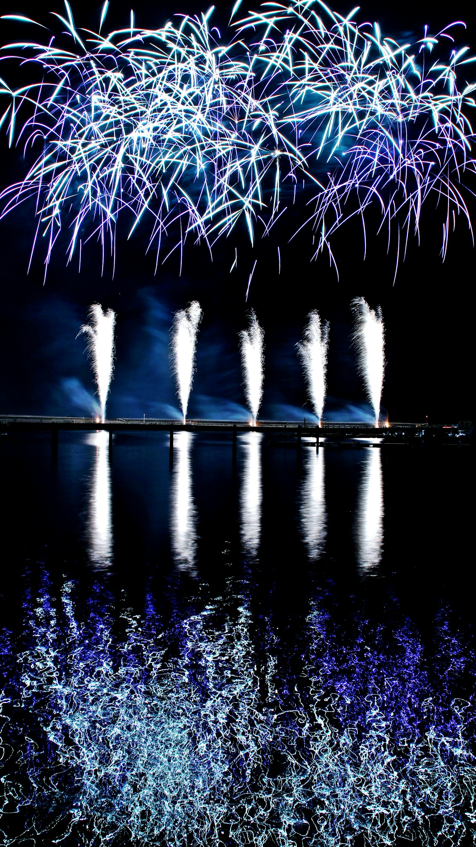 Fuochi d'artificio blu che illuminano il cielo notturno con bellissimi riflessi sull'acqua