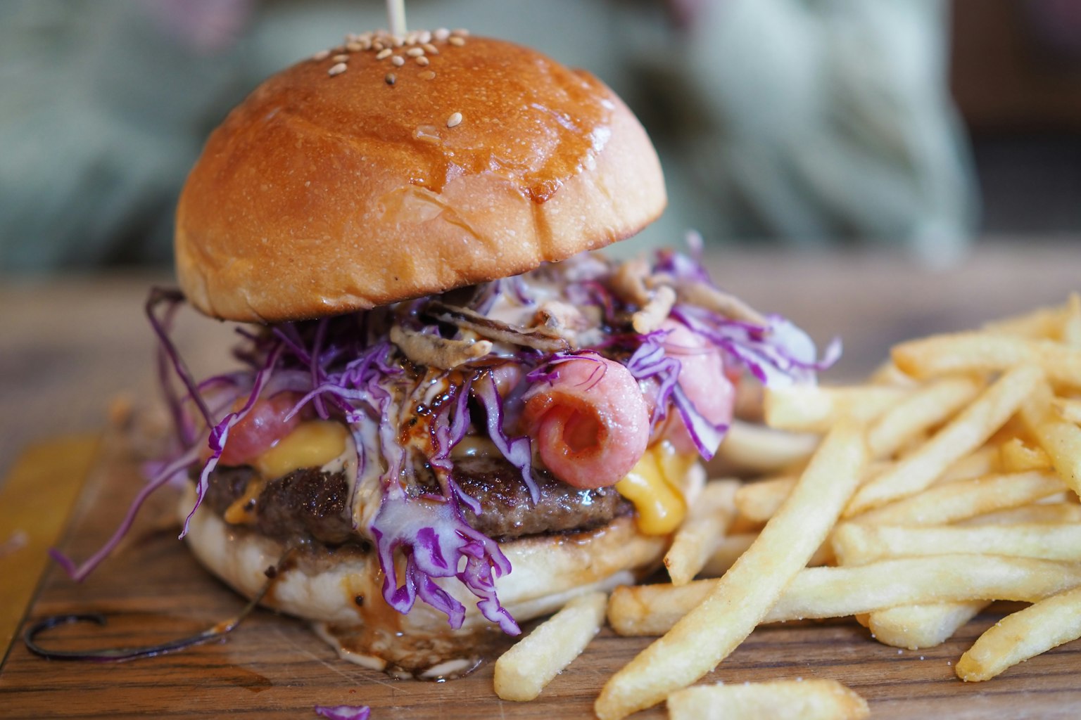 Juicy hamburger with purple cabbage and fries on a wooden board