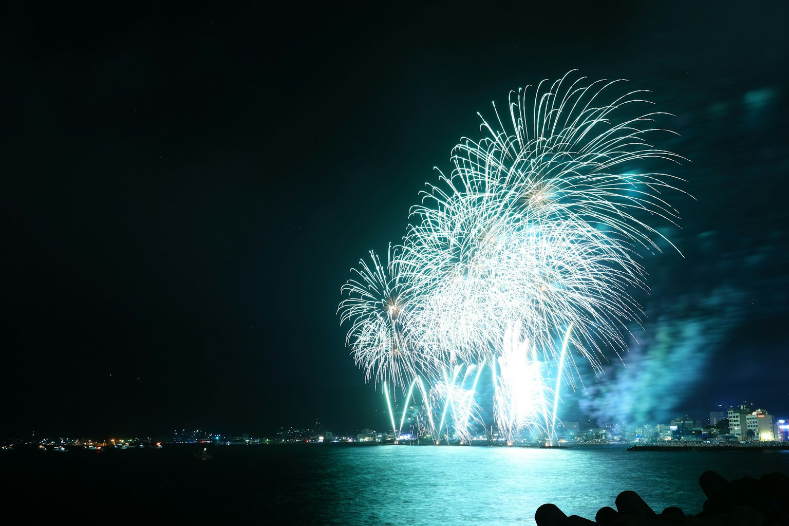 Bellissimo spettacolo di fuochi d'artificio che illumina il cielo notturno con riflessi sul mare