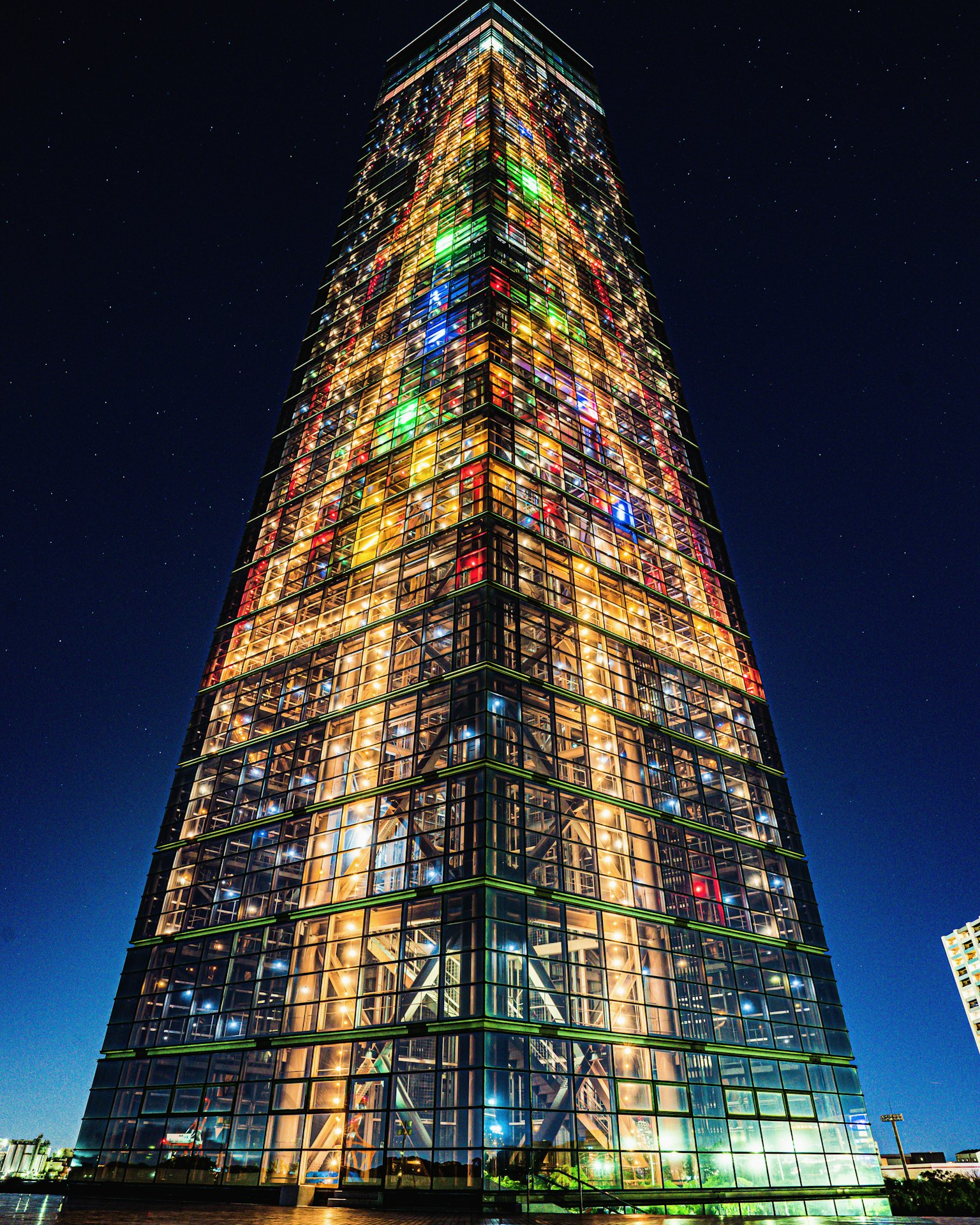 Farbenfrohes beleuchtetes Hochhaus bei Nacht vor einem sternenklaren Himmel