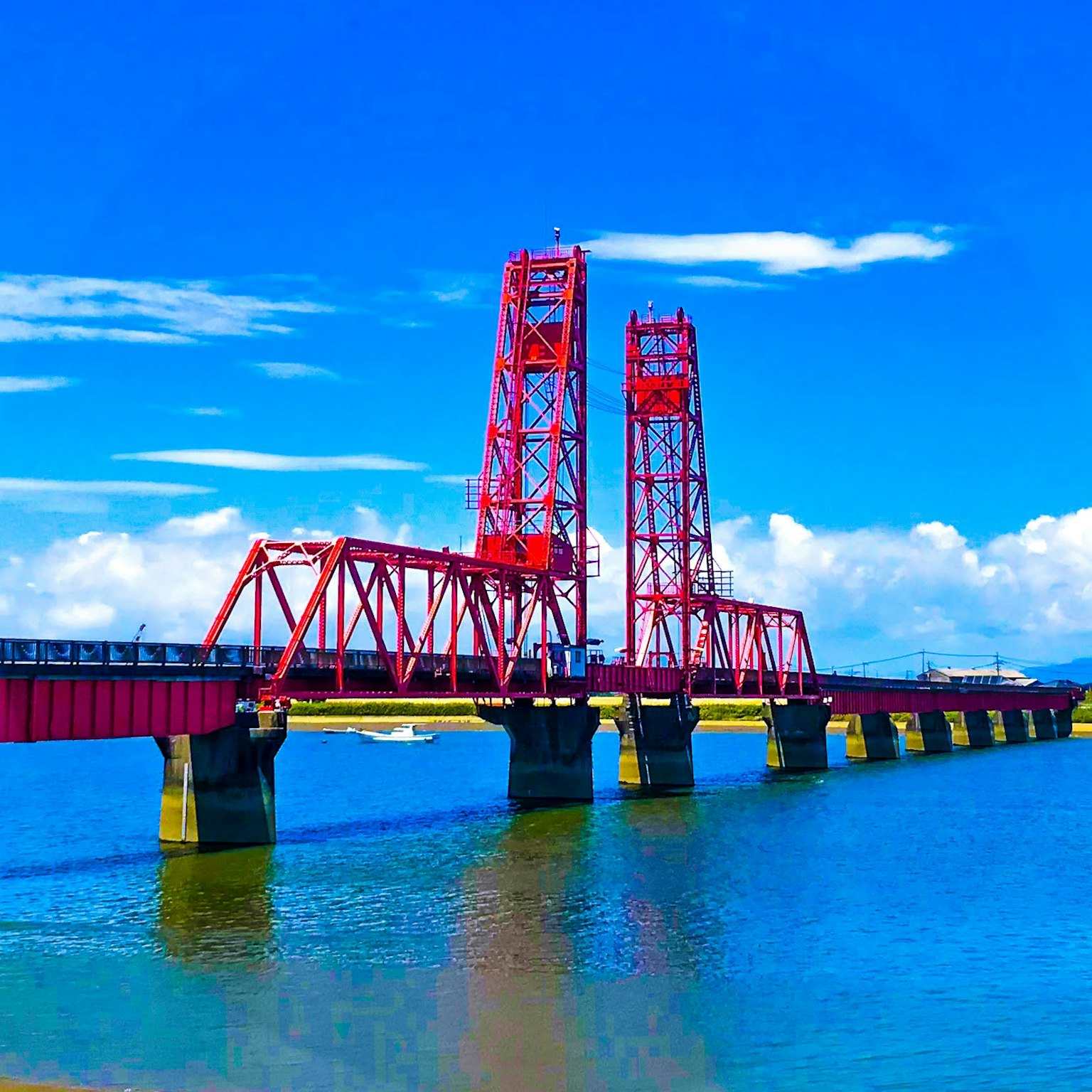Red steel bridge over calm blue water under a clear sky