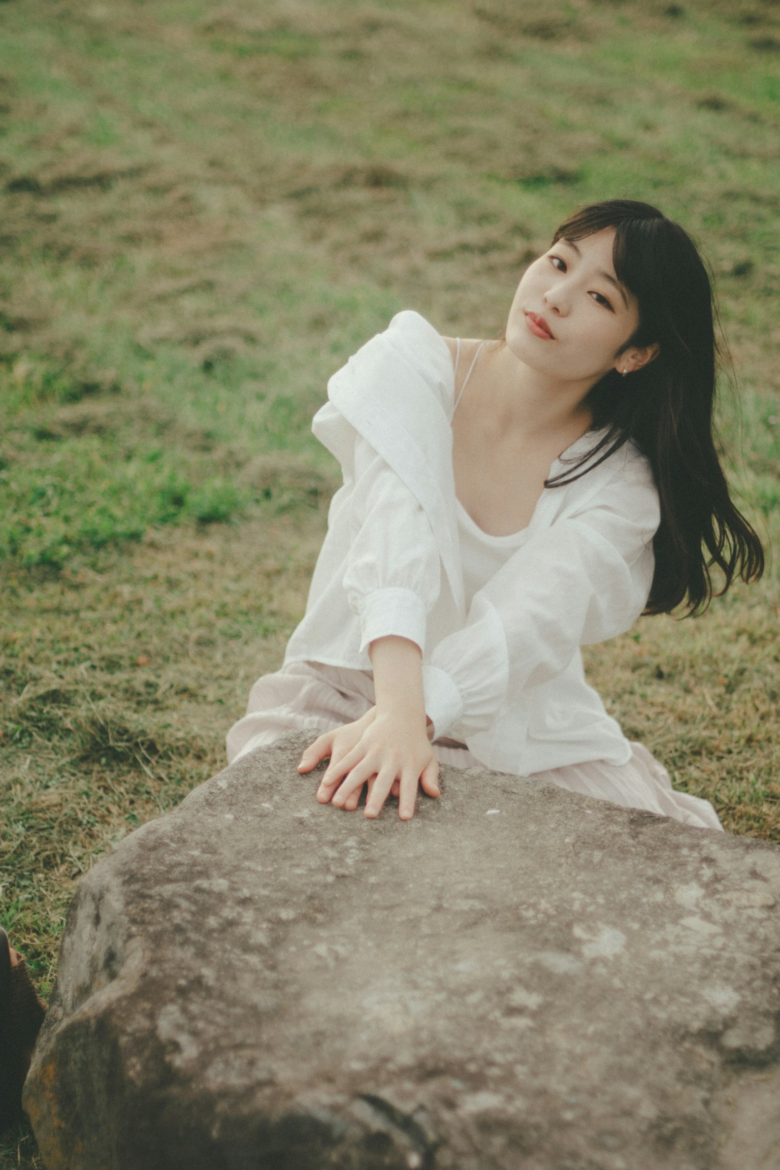 Portrait of a woman leaning on a stone in a grassy field wearing a white outfit