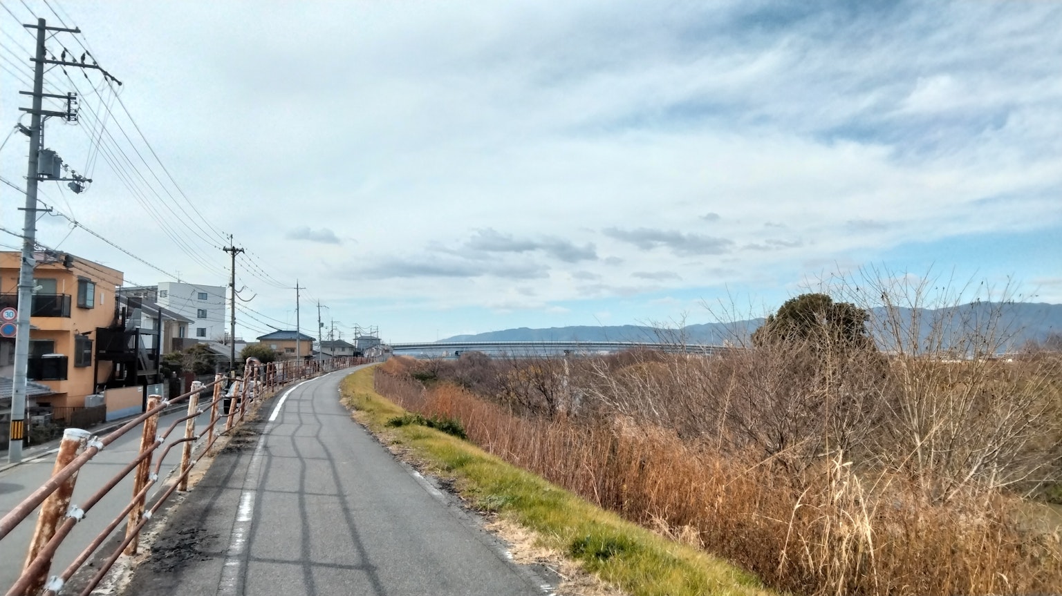 Route pittoresque au bord de la rivière avec des montagnes lointaines et un ciel nuageux