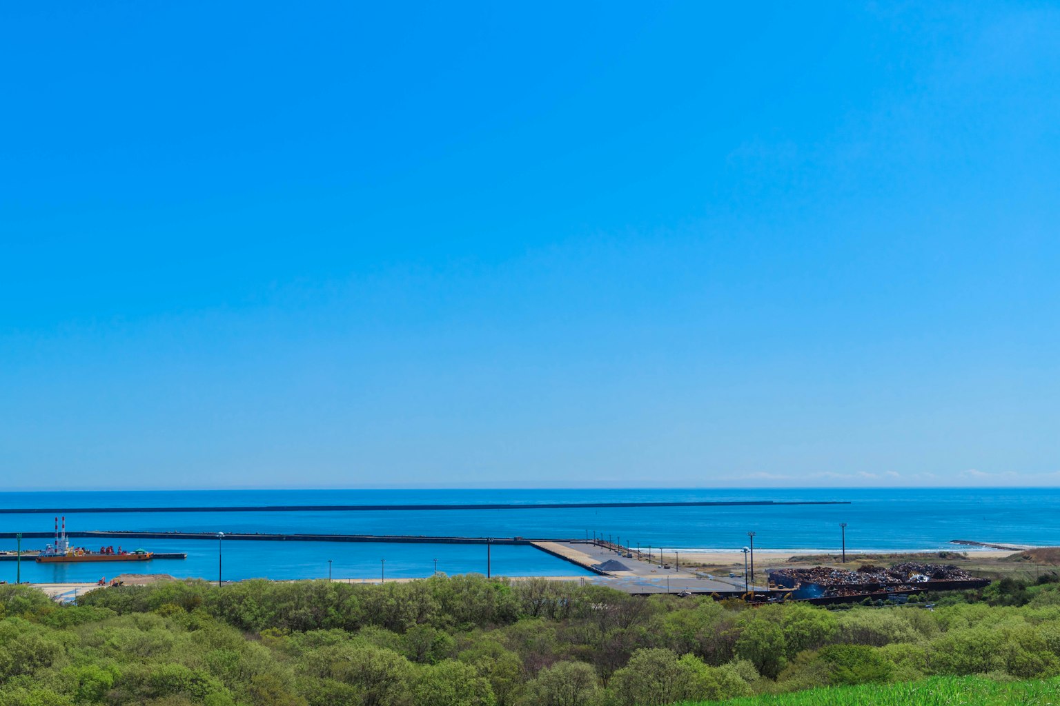 Vue panoramique d'un port avec mer et ciel bleus collines vertes au premier plan