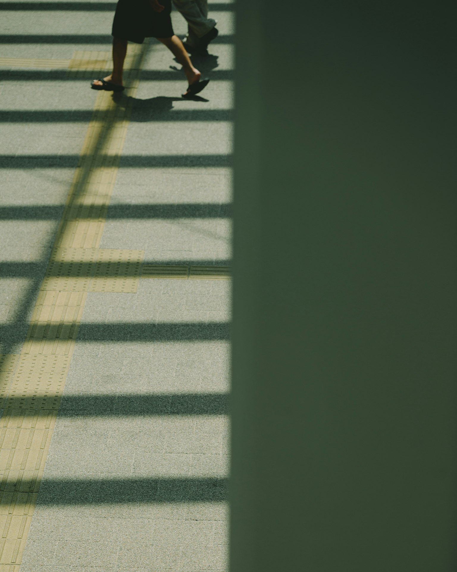 Eine Person, die im Schatten mit deutlich erkennbaren Streifen auf dem Boden geht
