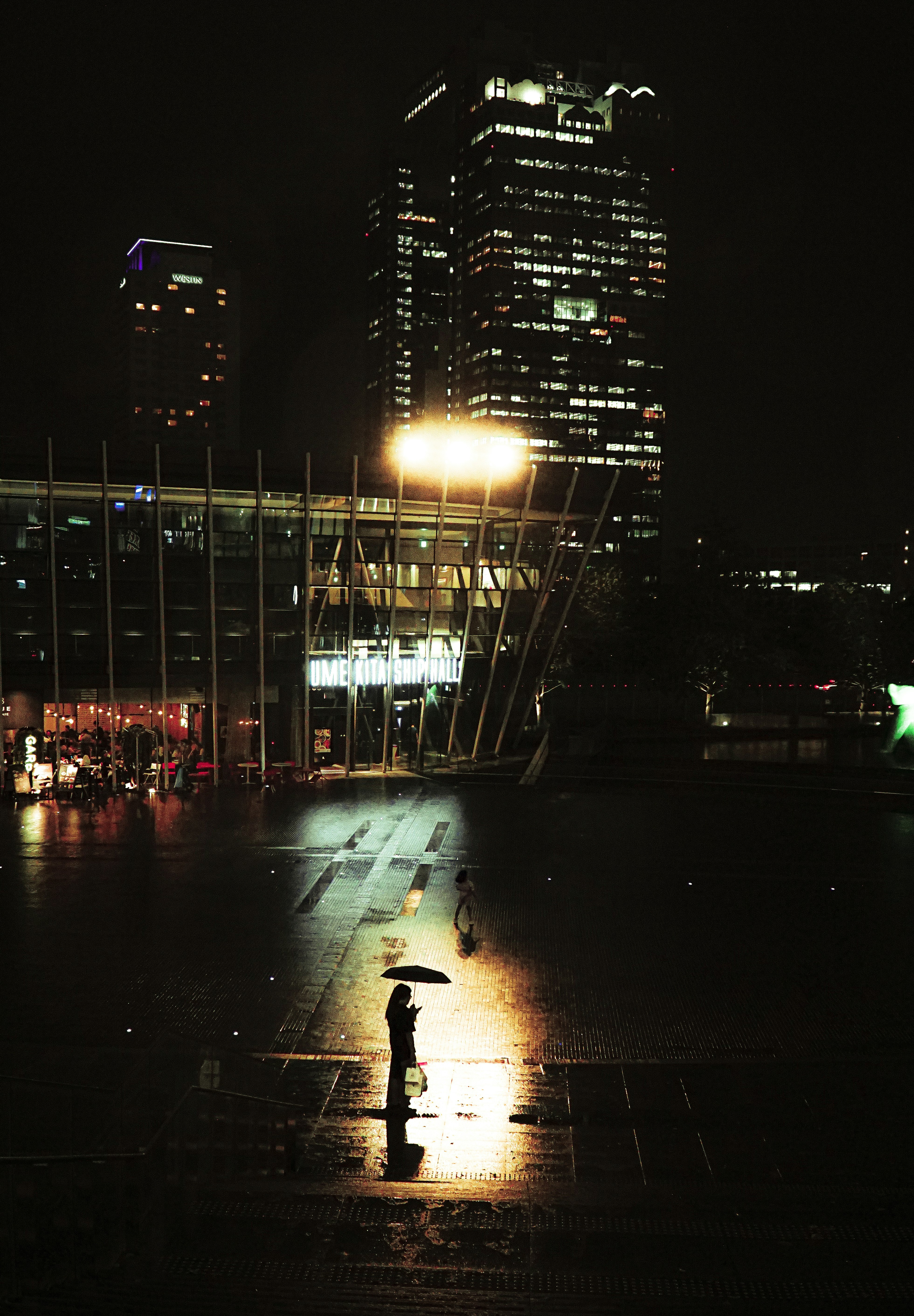 夜の雨上がりの大通りを歩く人と高層ビルの夜景