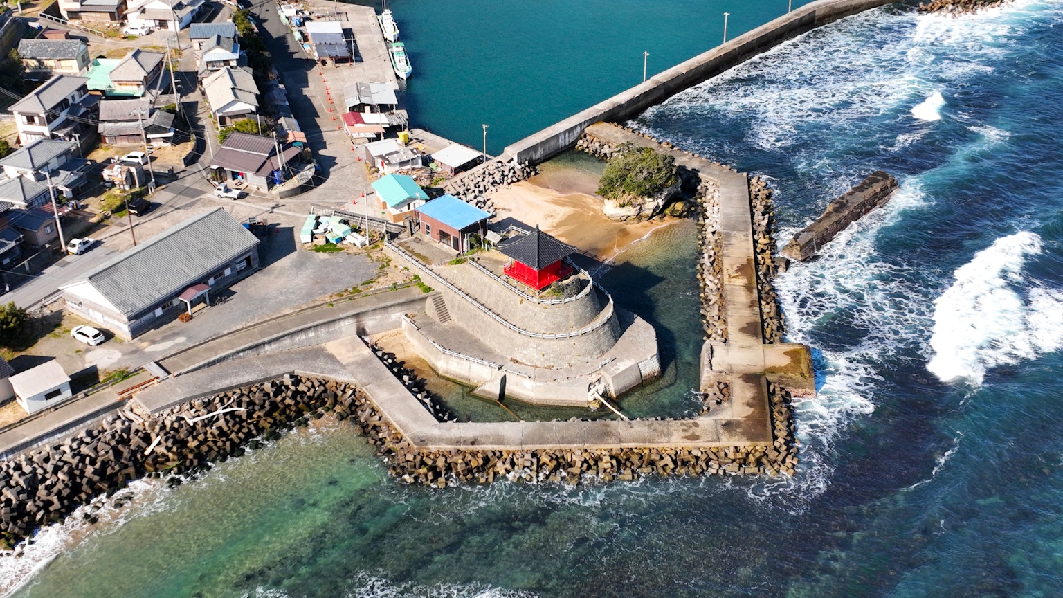 海岸小鎮的鳥瞰圖，紅頂燈塔和拍打岸邊的海浪