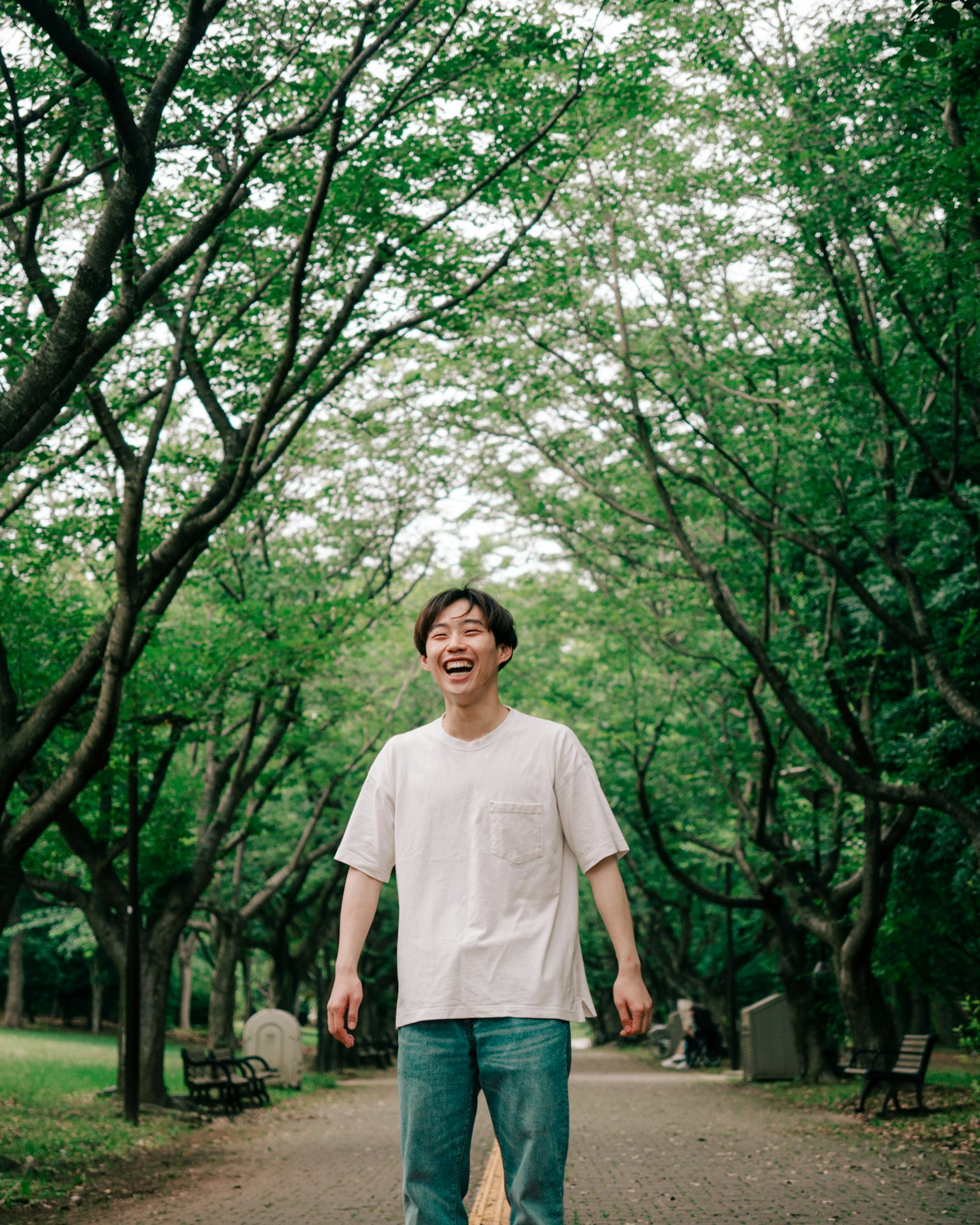 一名微笑的男子站在綠樹環繞的公園裡