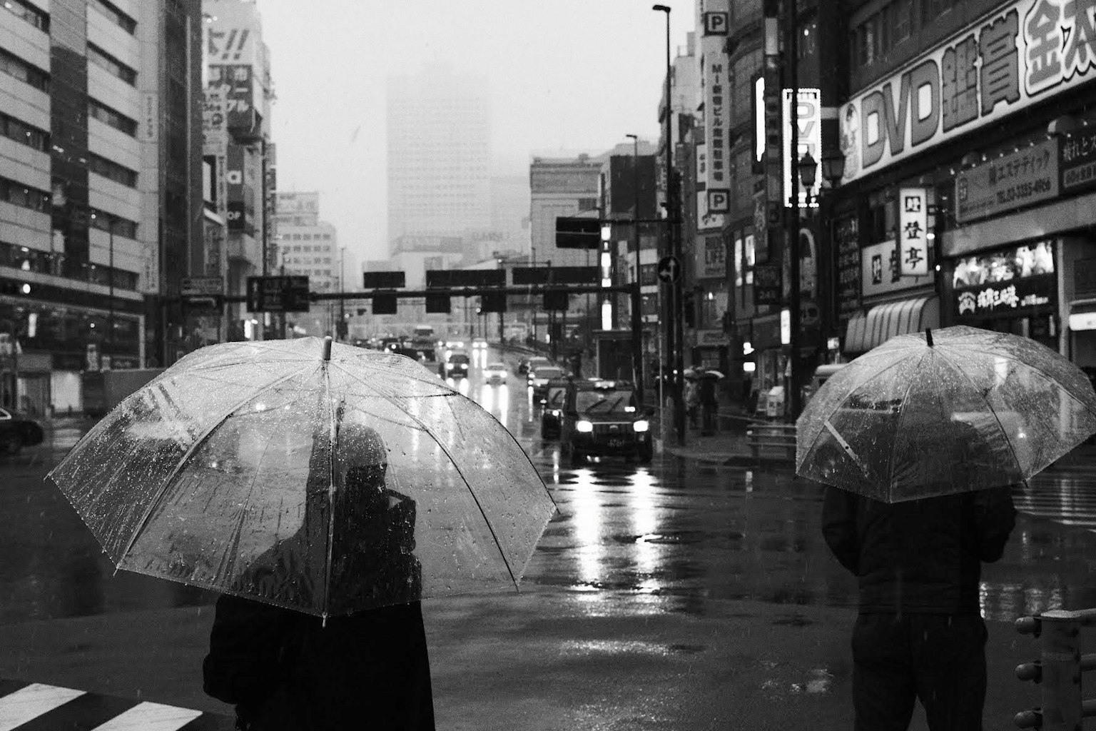Two people holding transparent umbrellas standing at a crosswalk in the rain