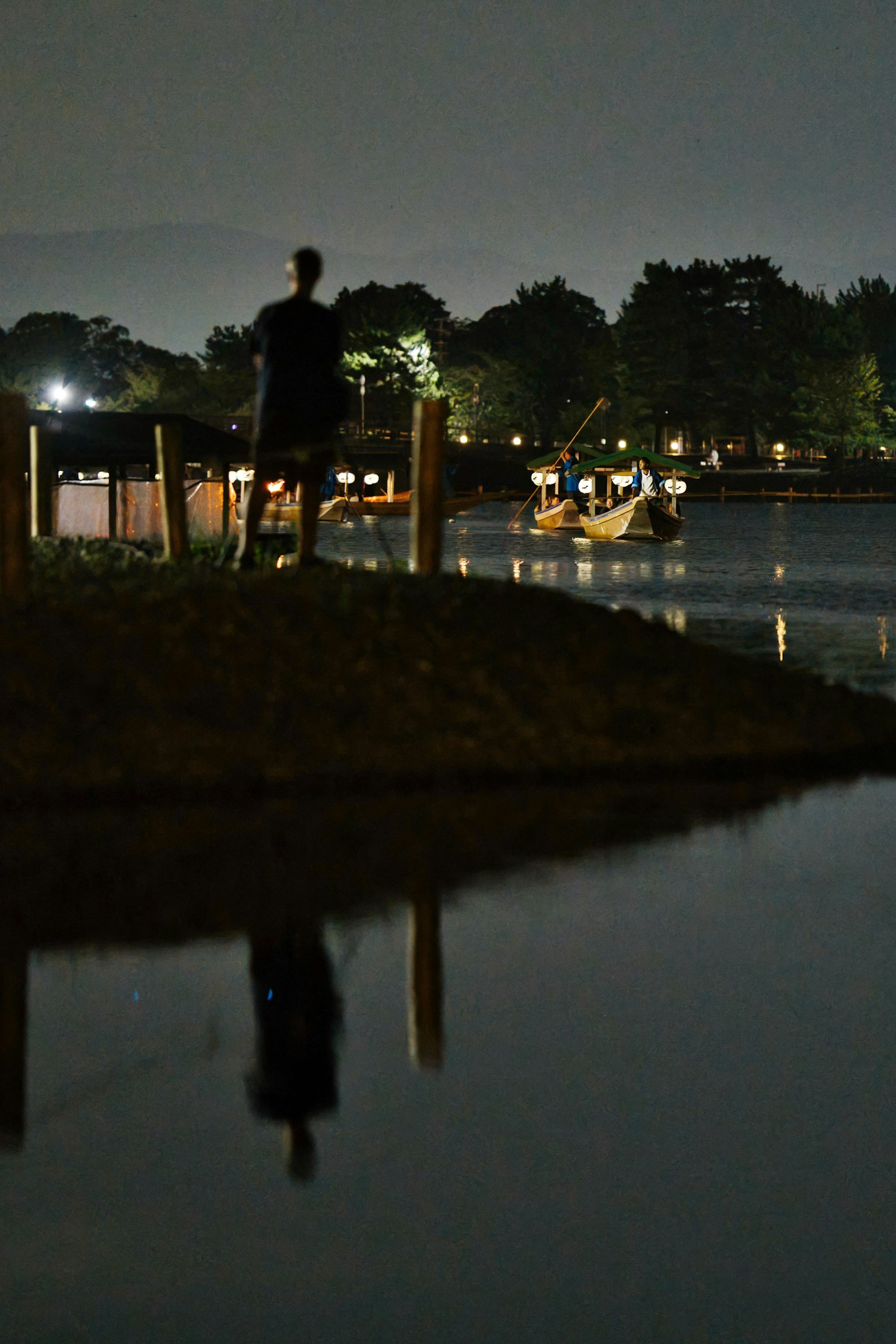Silueta de una persona de pie junto a un lago por la noche con reflejo en el agua