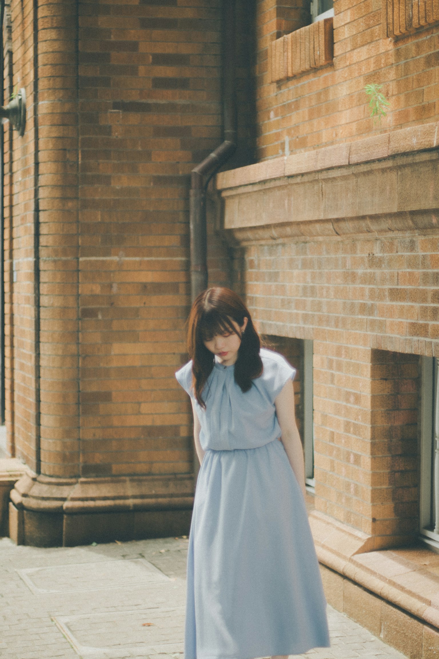 Femme en robe bleue se tenant devant un mur en briques
