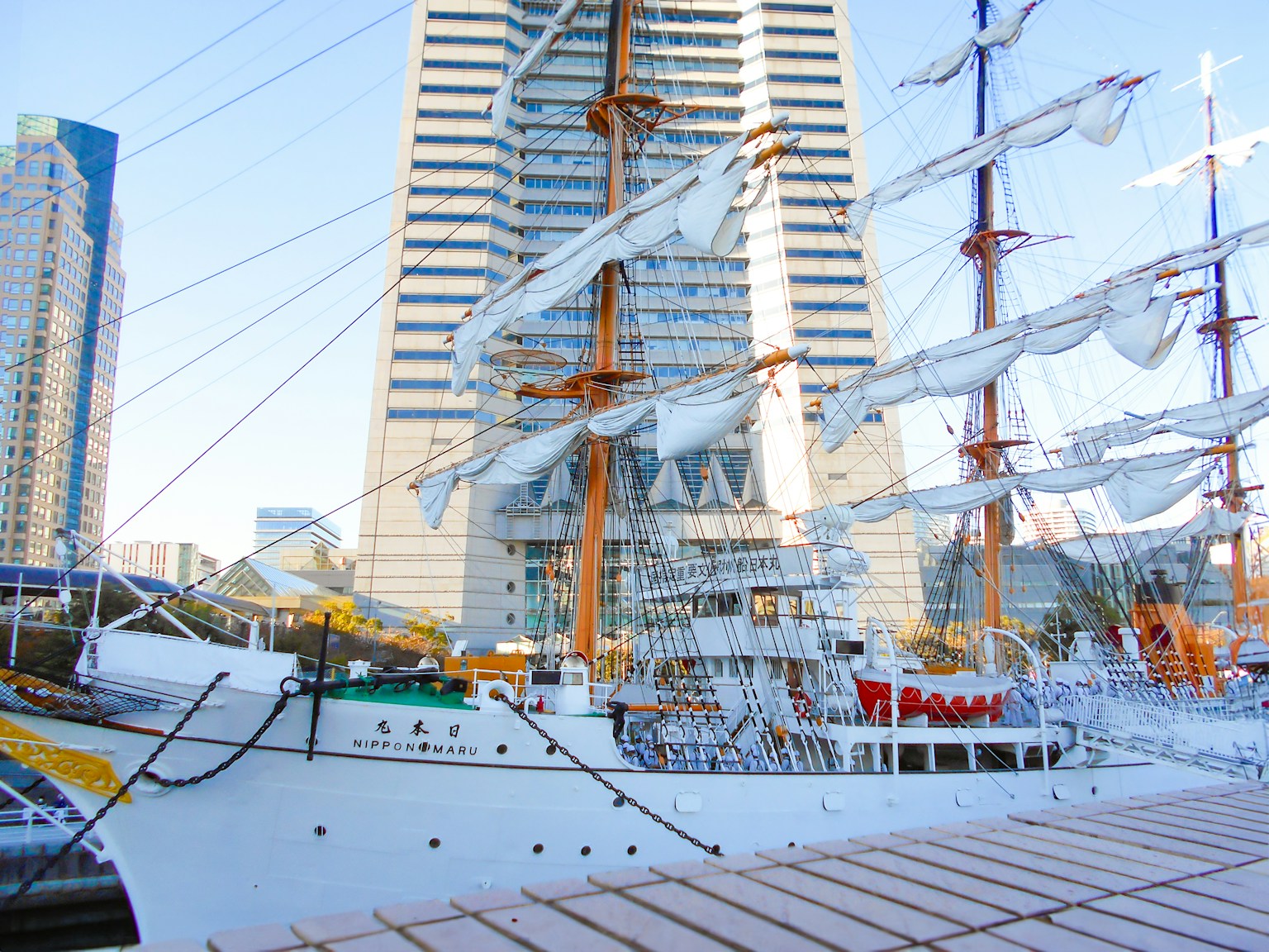 Large white-sailed ship docked beside modern skyscrapers