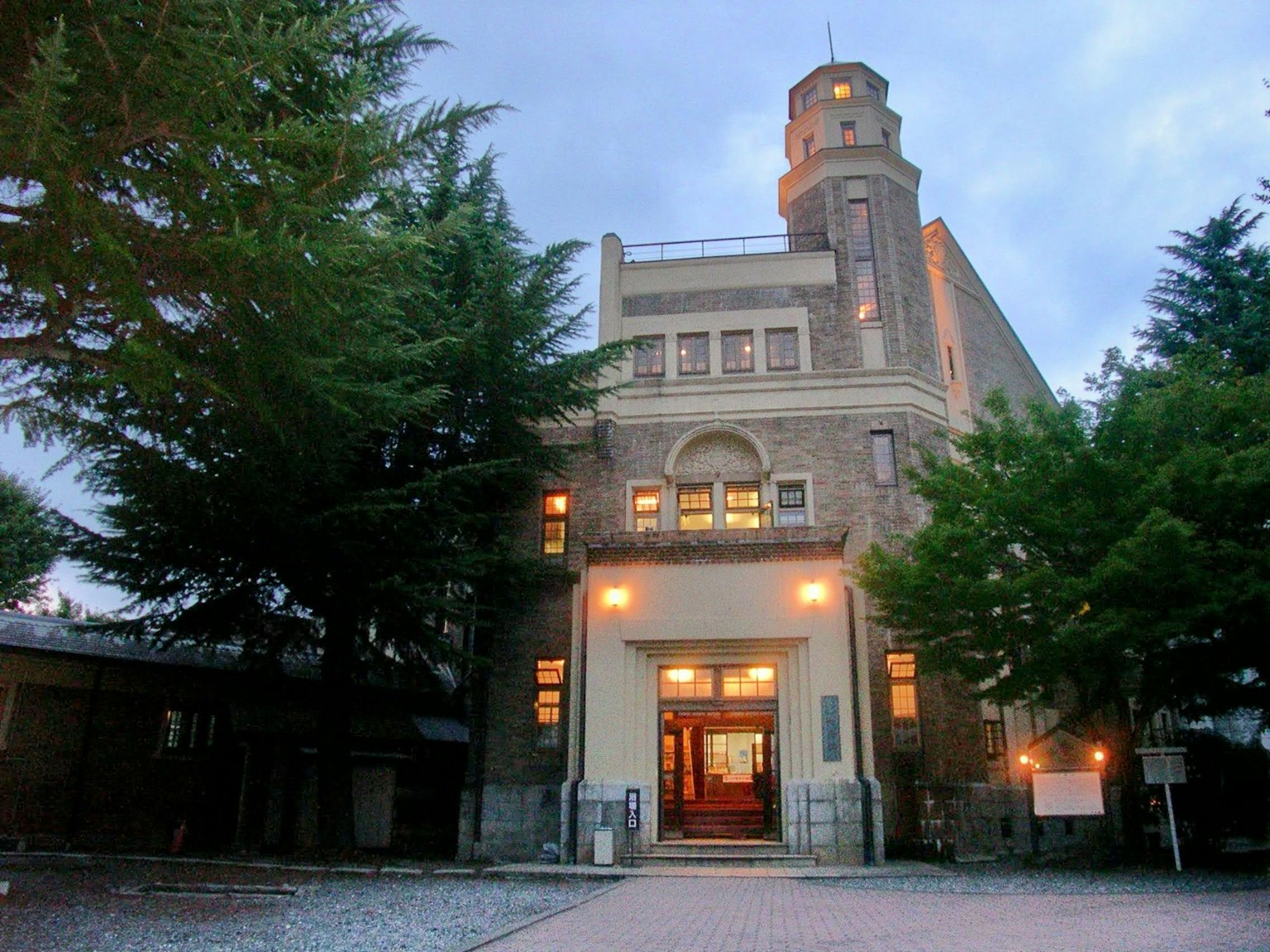 Esterno di un edificio storico illuminato al crepuscolo circondato da alberi verdi con una torre distintiva