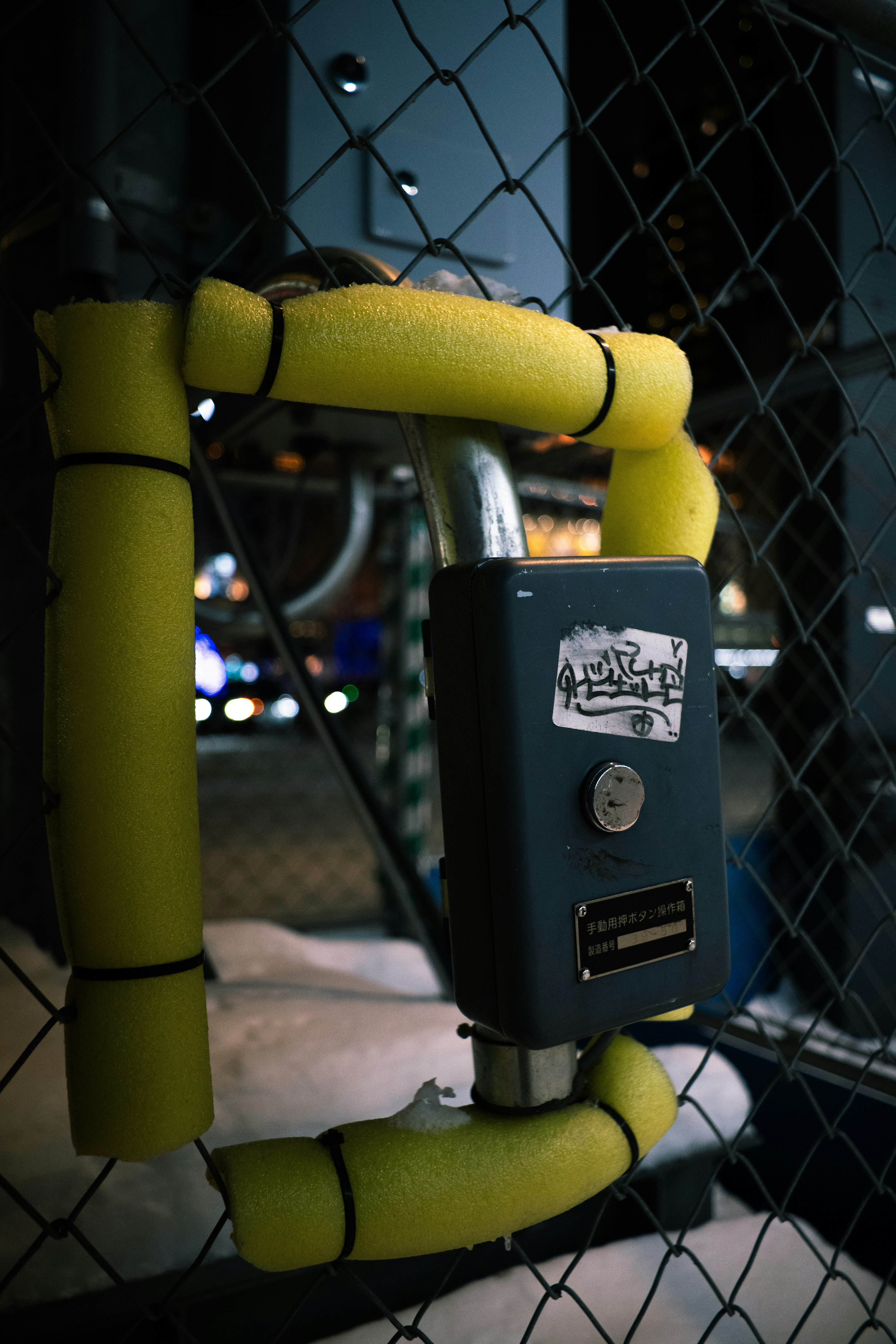 Un passage avec des tuyaux jaunes et un boîtier de machine visibles à travers une clôture
