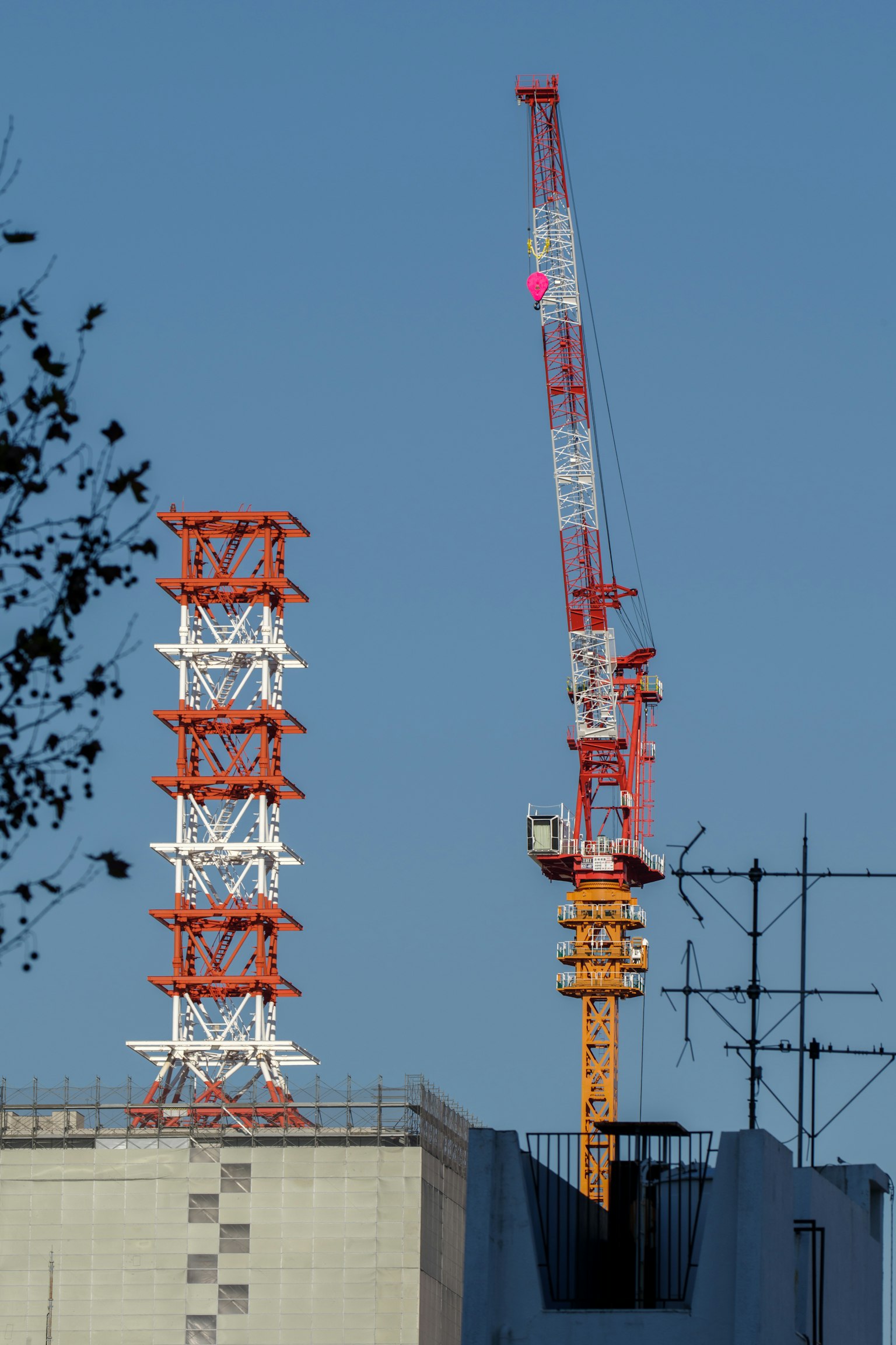 Orange Baukran und rot-weißer Sendemast unter blauem Himmel