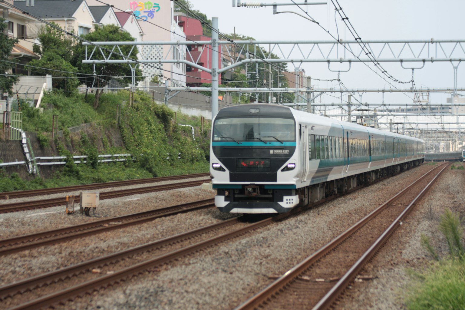 Ein weißer und grüner Zug fährt auf Gleisen mit einem Hintergrund aus Bahninfrastruktur und Gebäuden