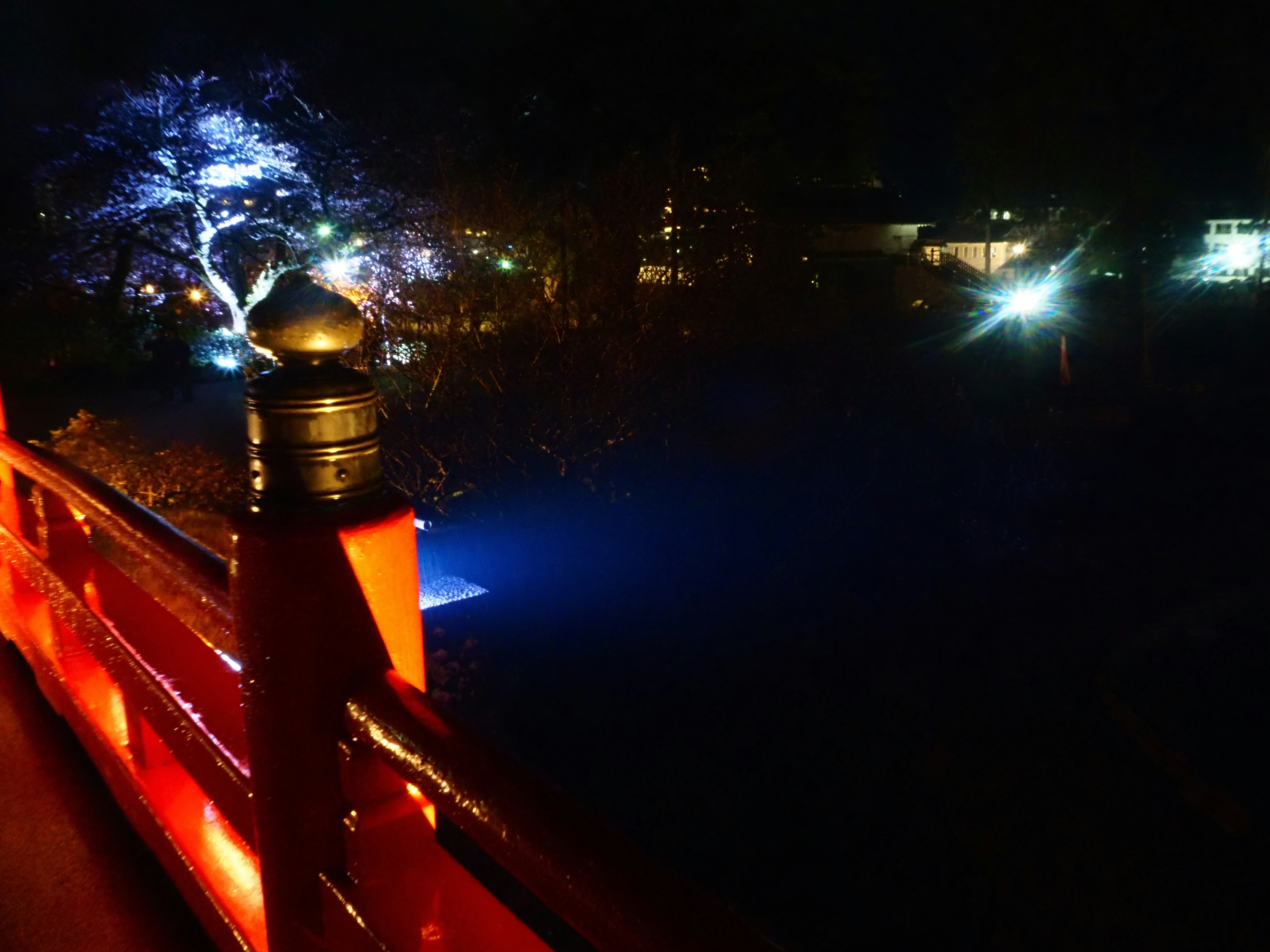 夜の橋の手すりと街灯の光がにじむ川沿いの風景