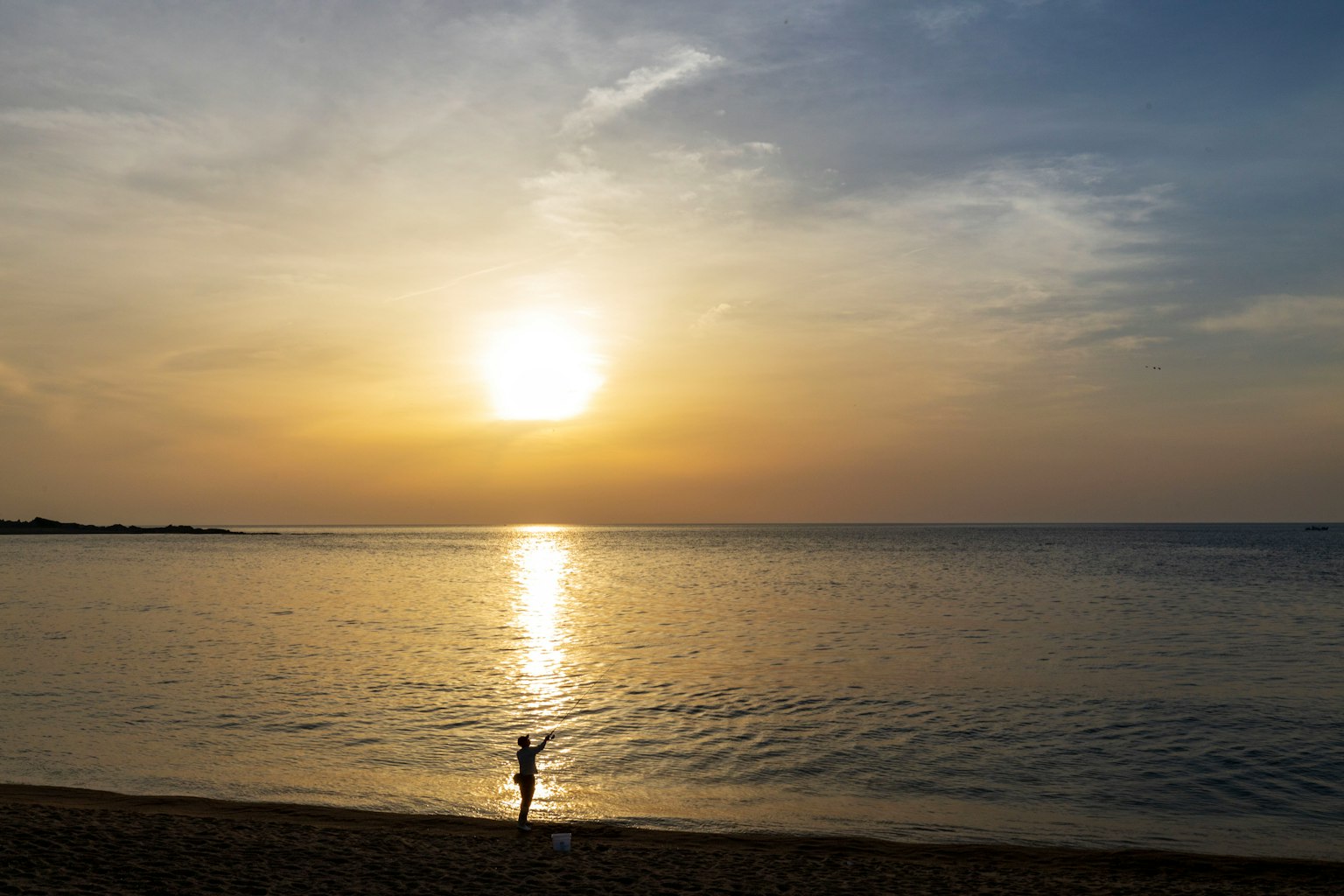 Une personne debout sur la plage avec un coucher de soleil en arrière-plan se reflétant sur l'eau