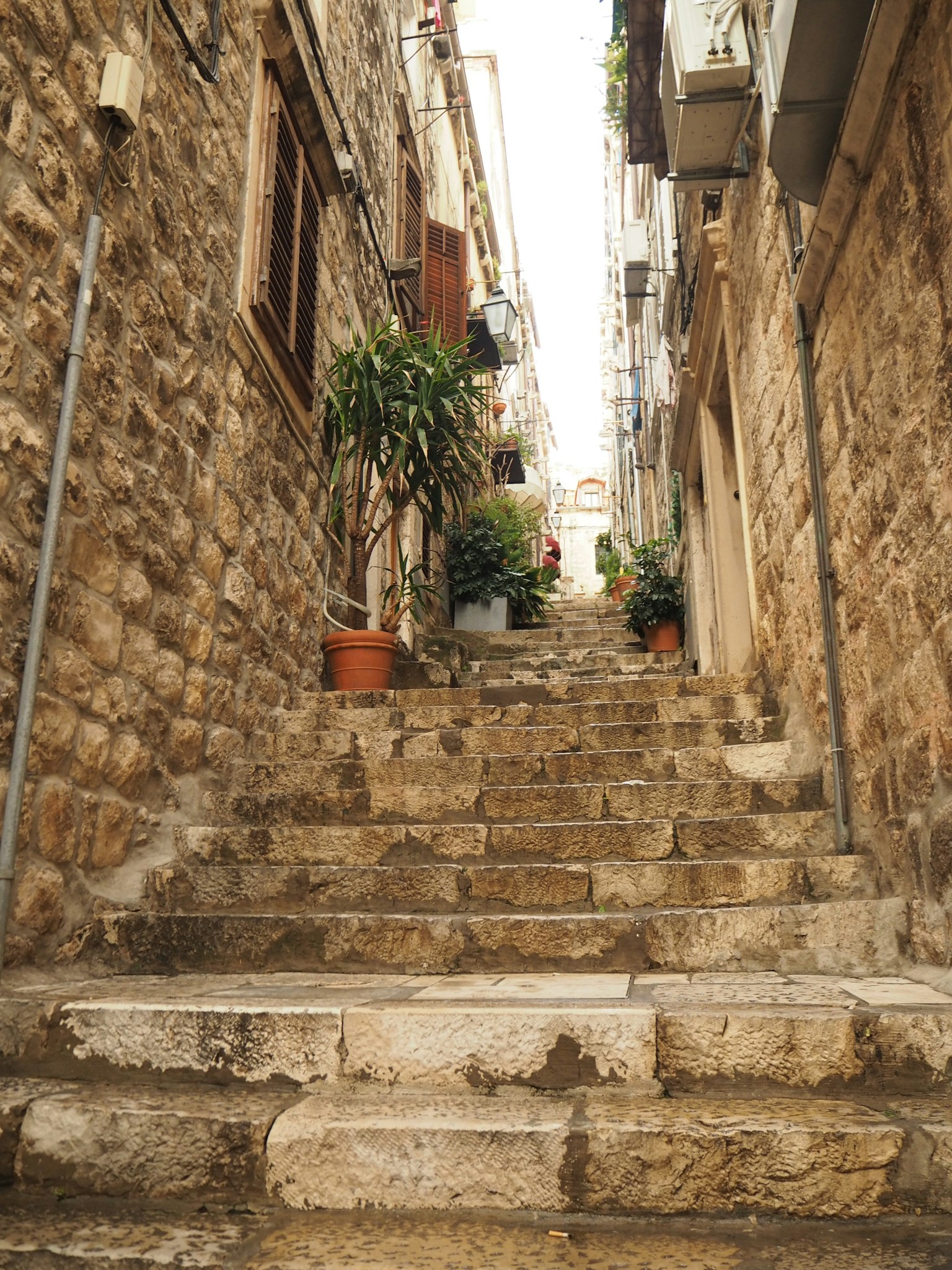 ตรอกแคบที่มีบันไดหินเก่าและกระถางดอกไม้สองข้าง