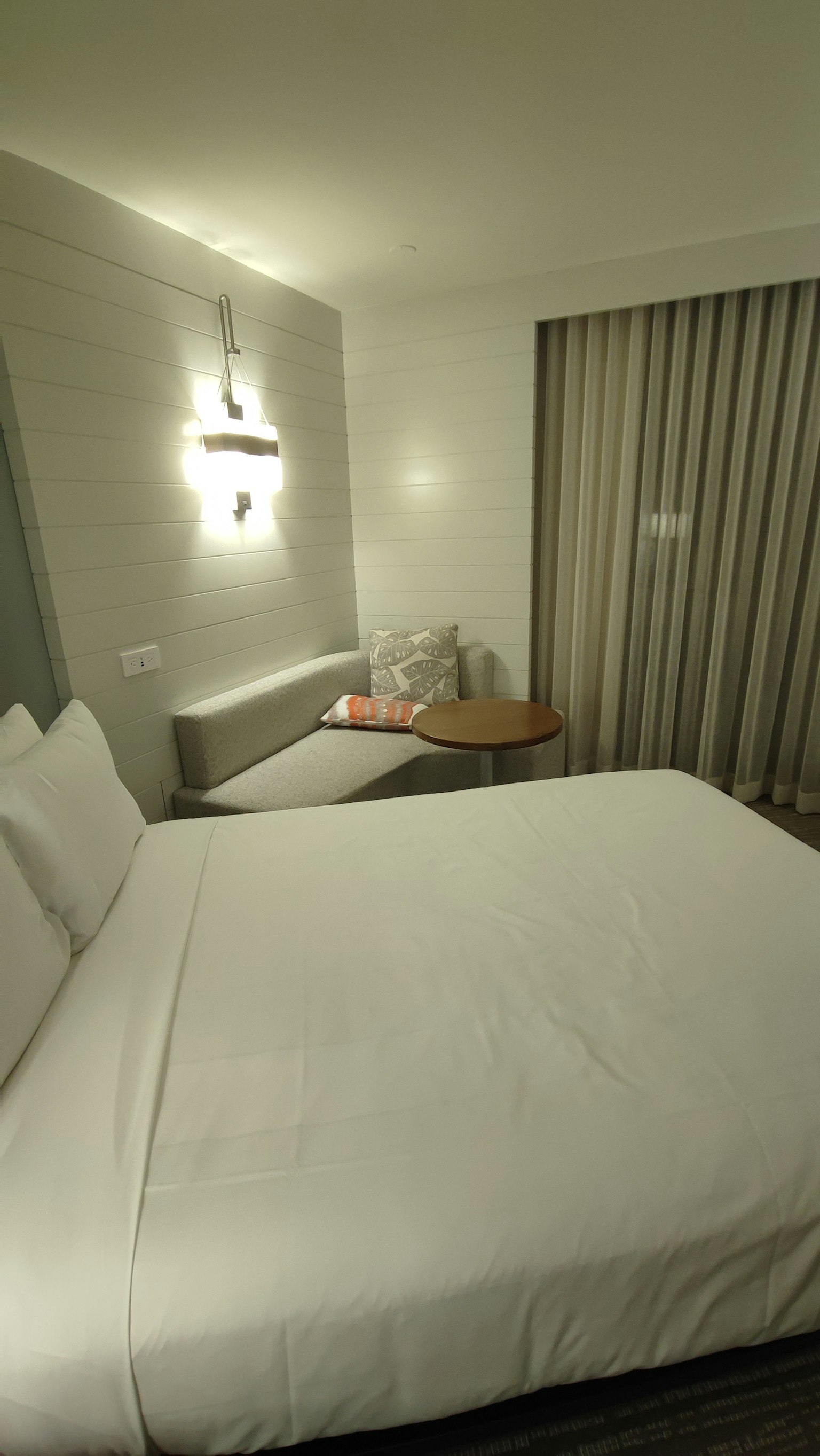 Kamar hotel modern dengan tempat tidur putih dan bantal lembut pencahayaan dinding dan tirai di jendela